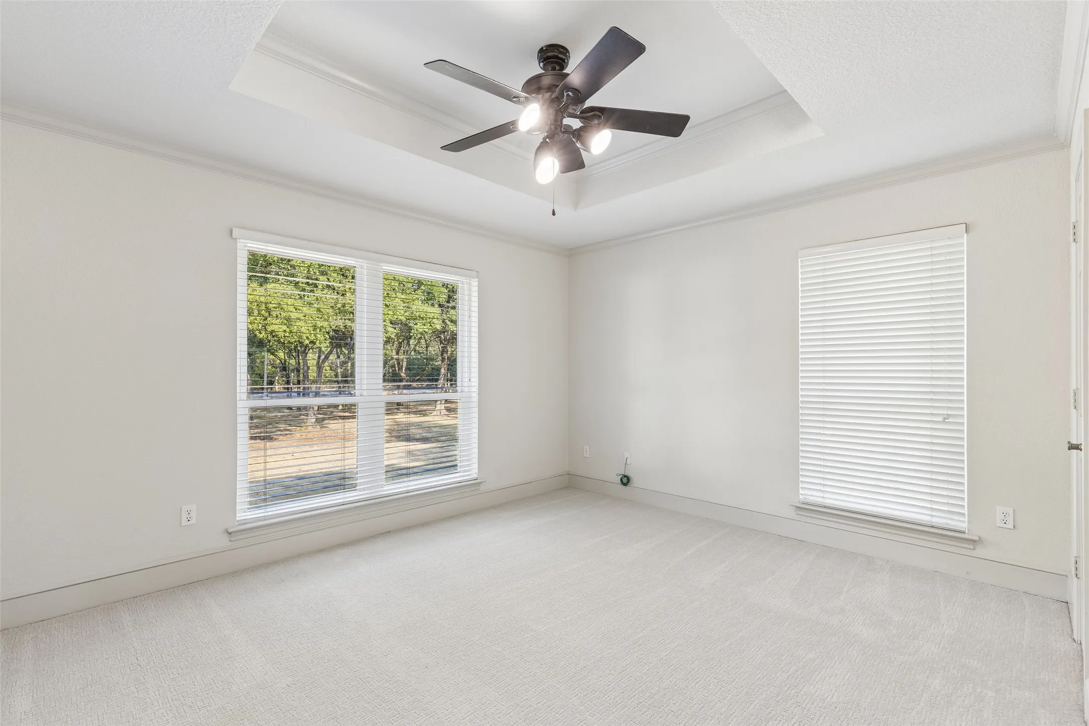 Recessed ceiling with a contemporary ceiling fan, white walls, and light-toned carpeting