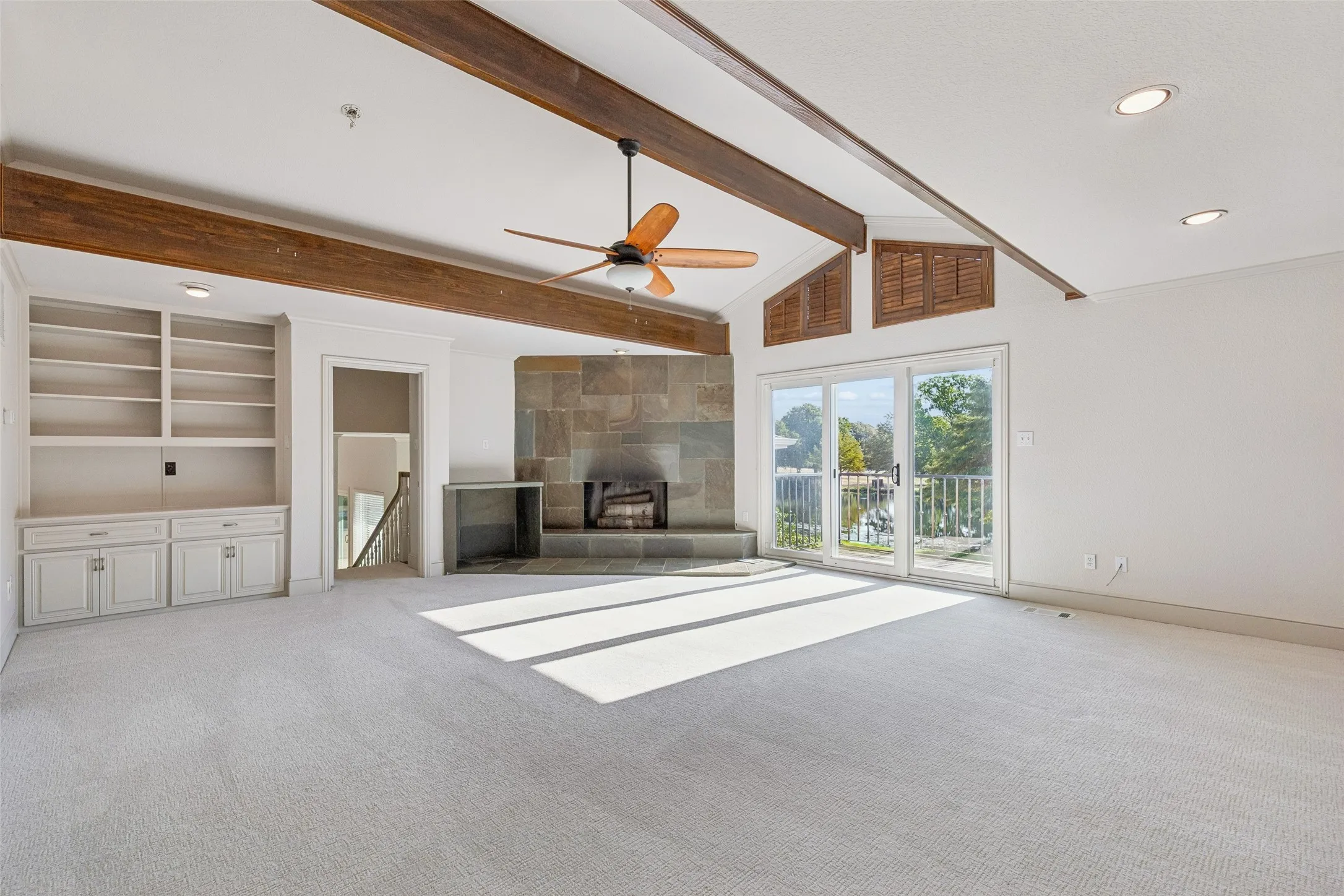 Vaulted ceiling with exposed wood beams, built-in shelving, stone-faced fireplace, and sliding glass doors to outdoor space