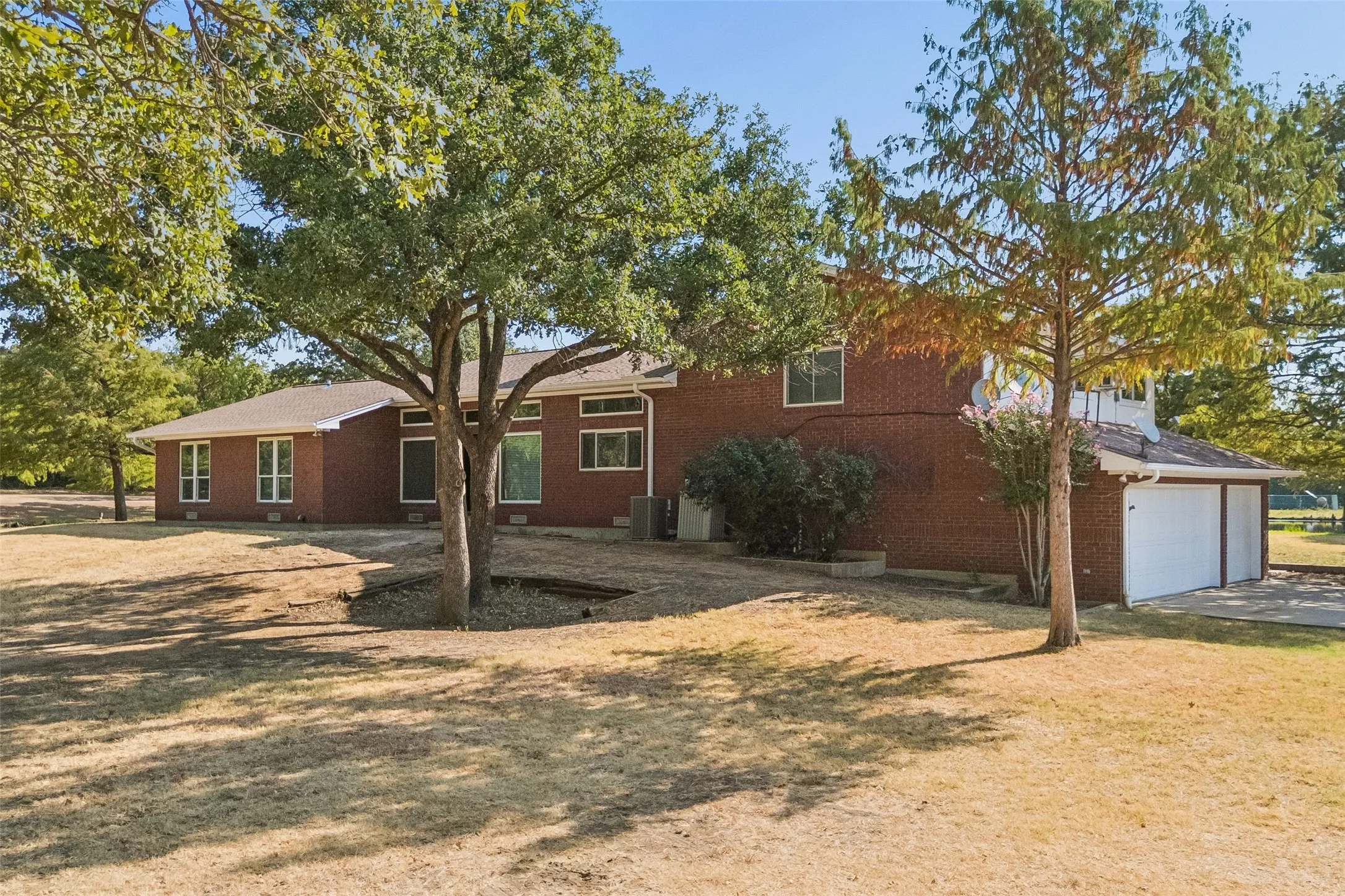 Brick exterior with white frame windows, attached two-car garage, and mature trees