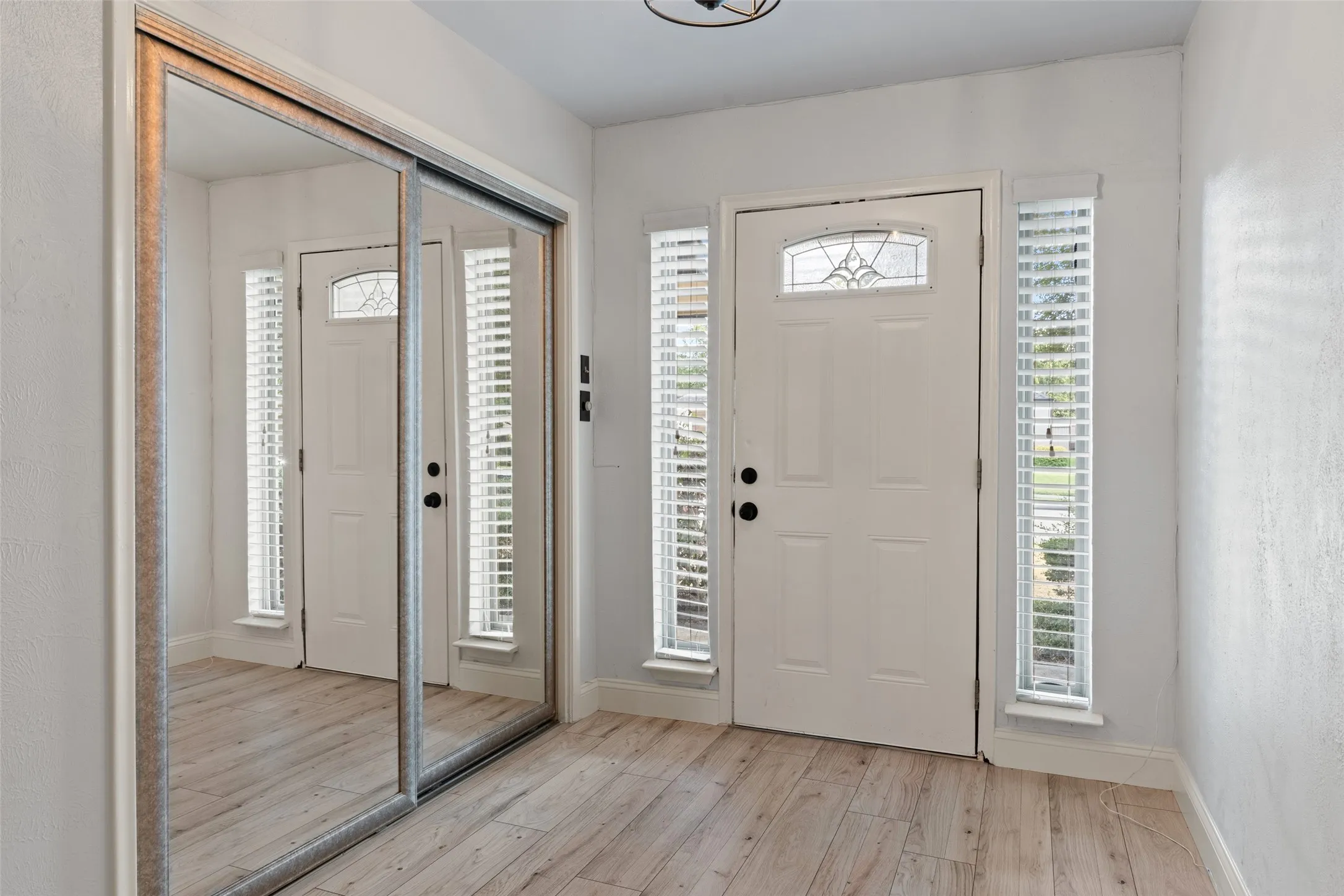 Entryway featuring wood-finish flooring, a paneled door with leaded glass insert, and sidelight windows with blinds