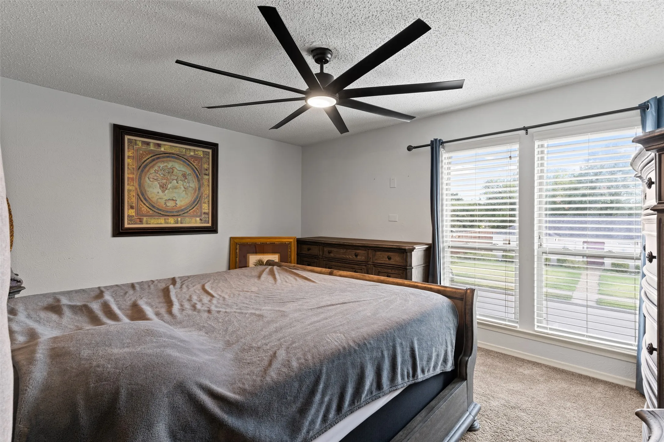 Ceiling fan with multiple blades, soft white walls, two windows with blinds, and neutral carpeting