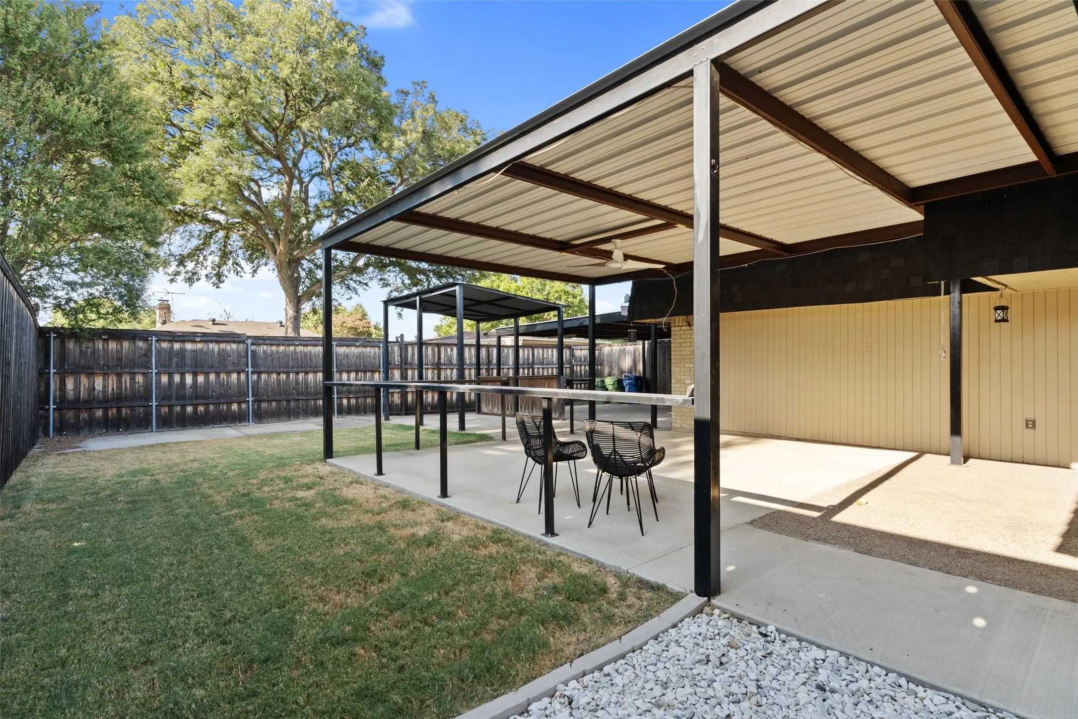 Covered patio structure with metal roofing, concrete patio, and fenced perimeter