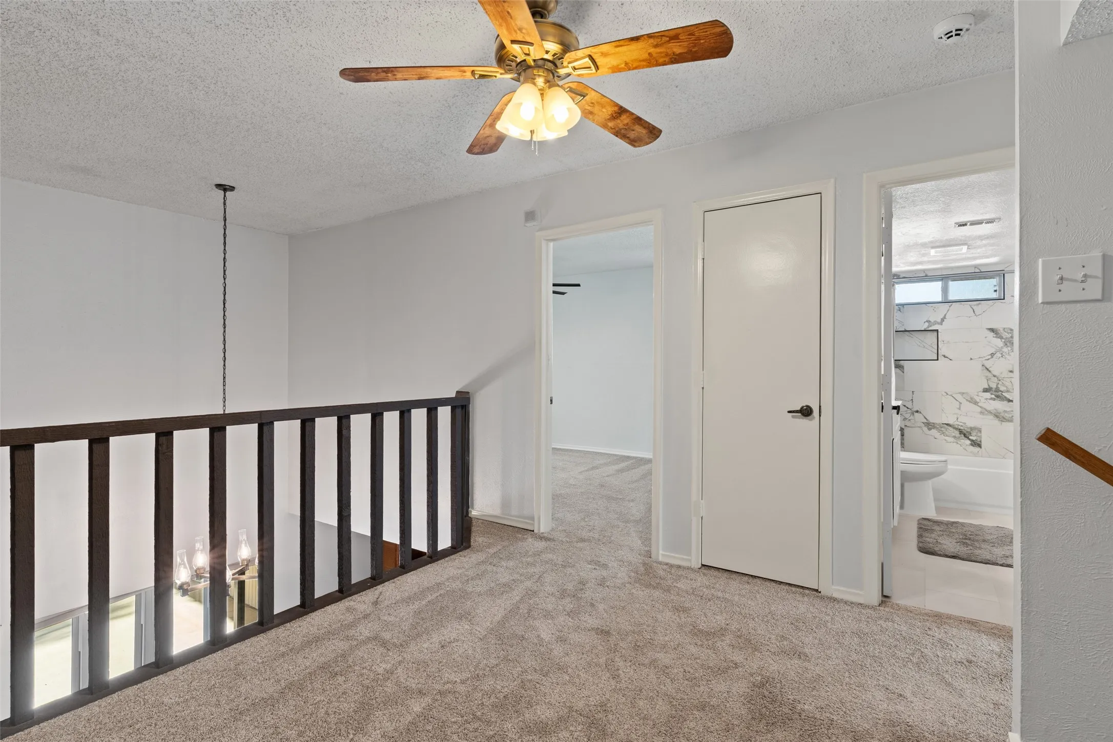 Carpeted landing with a ceiling fan, wood railing, and multiple doorways