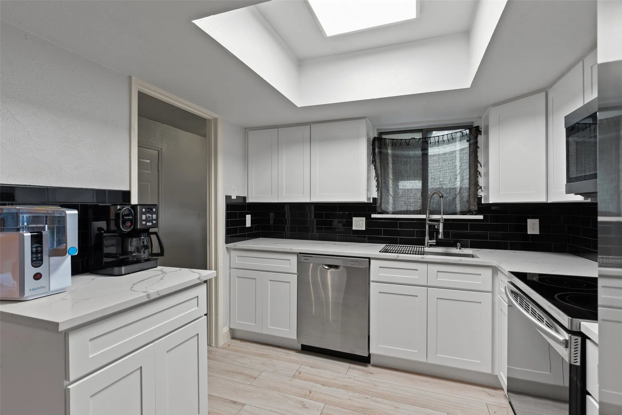 White shaker cabinetry with stone-finish countertops, black subway tile backsplash, stainless steel appliances, and a skylight