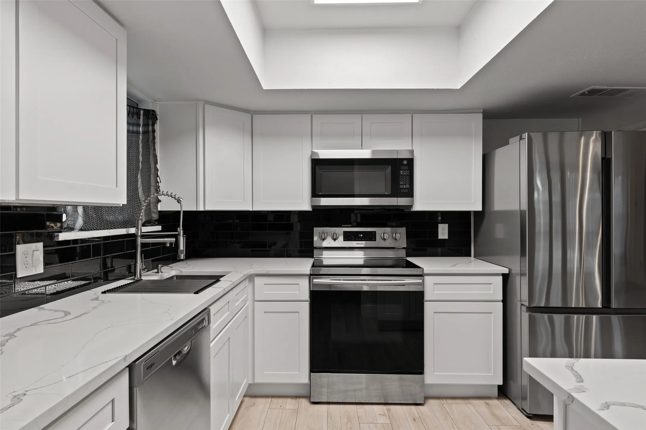 White cabinetry, stainless steel appliances, black subway tile backsplash, white countertops, and wood-finish flooring