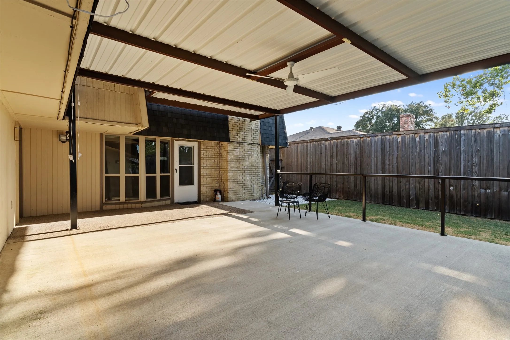 Expansive concrete patio with a metal roof overhang and an attached ceiling fan