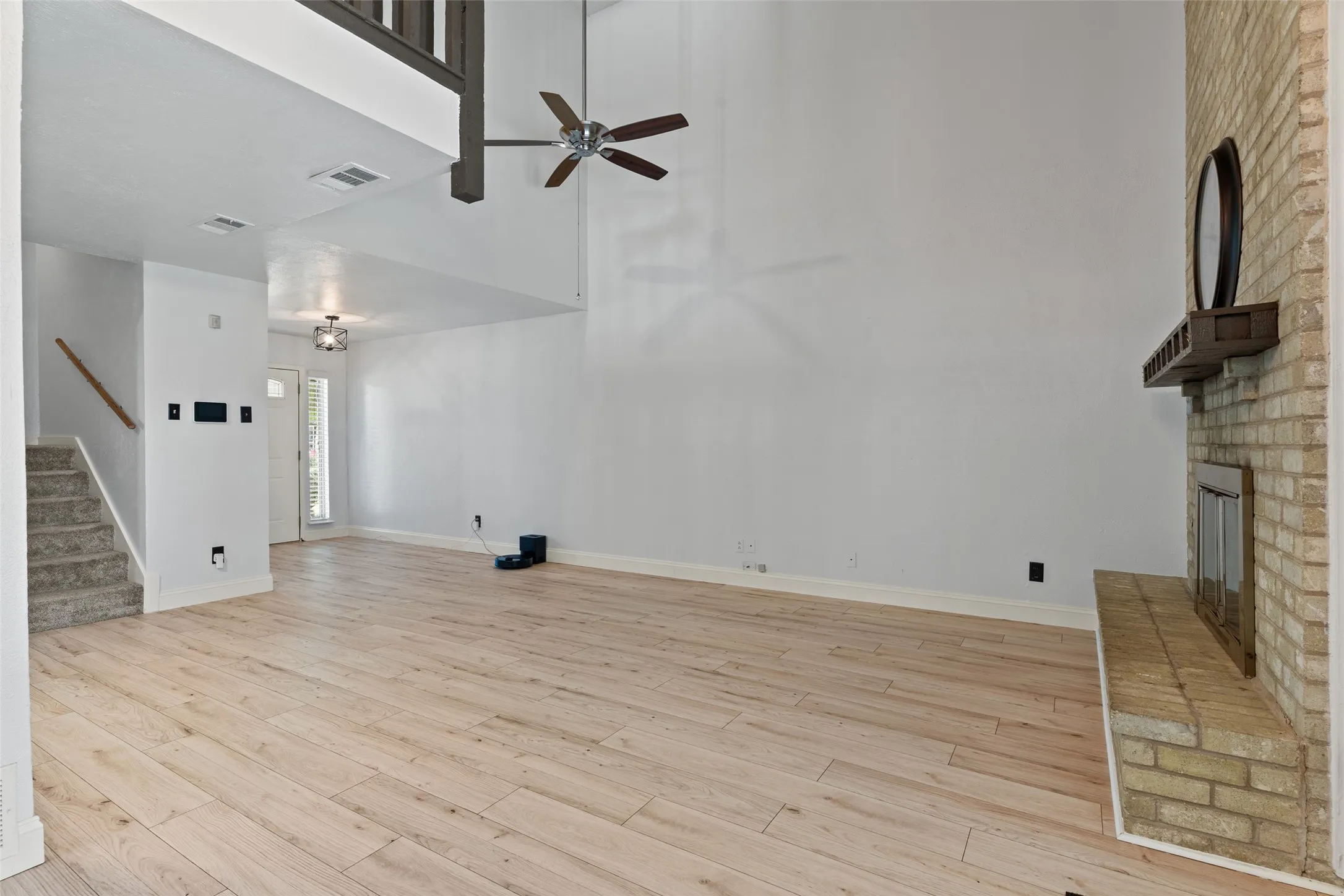 Vaulted ceilings with a ceiling fan, light wood-finish flooring, brick-faced fireplace with a wood mantle, and a carpeted staircase with a wood handrail