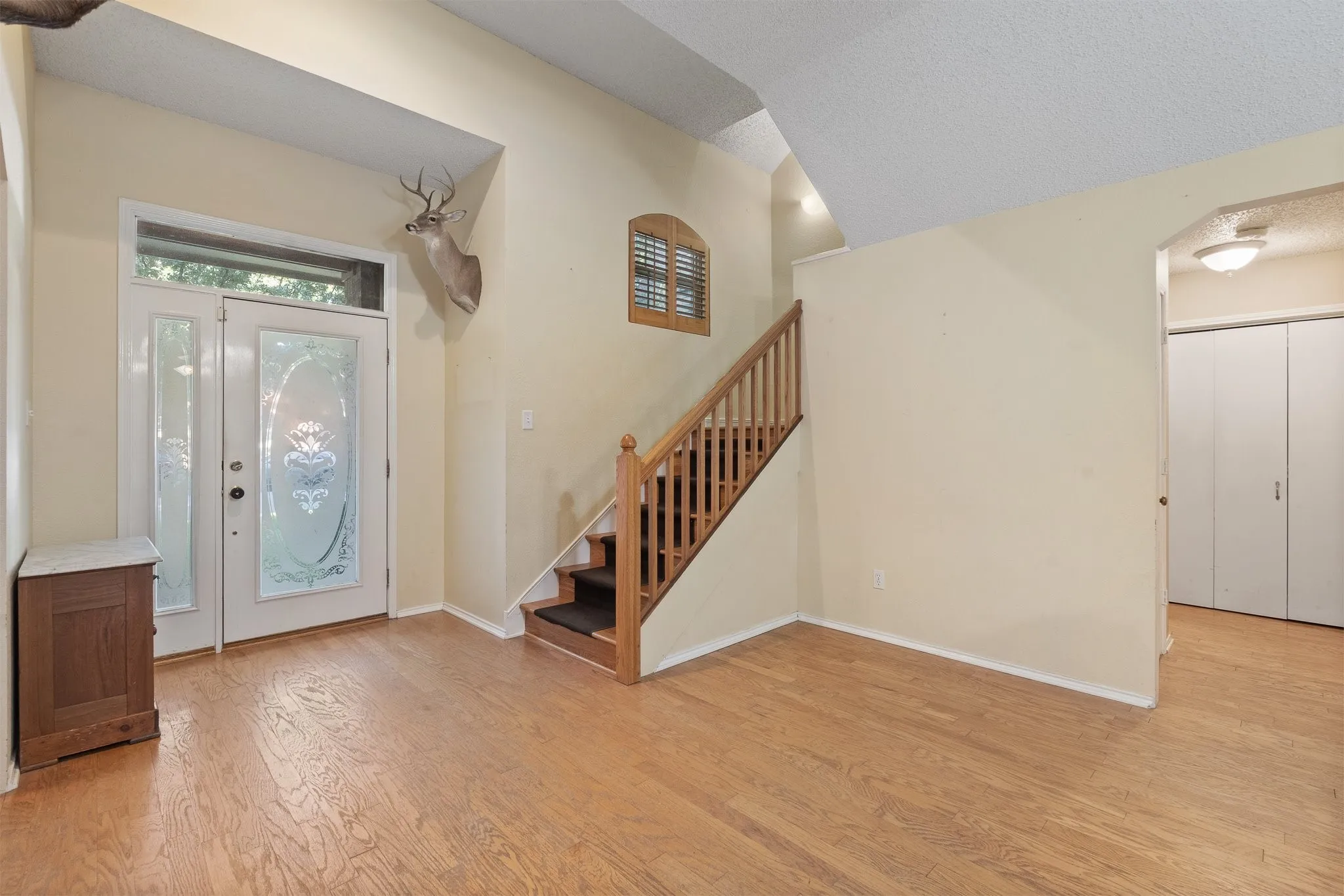 Wood-finish flooring throughout, white paneled entry door with decorative glass, and a natural wood staircase with balusters
