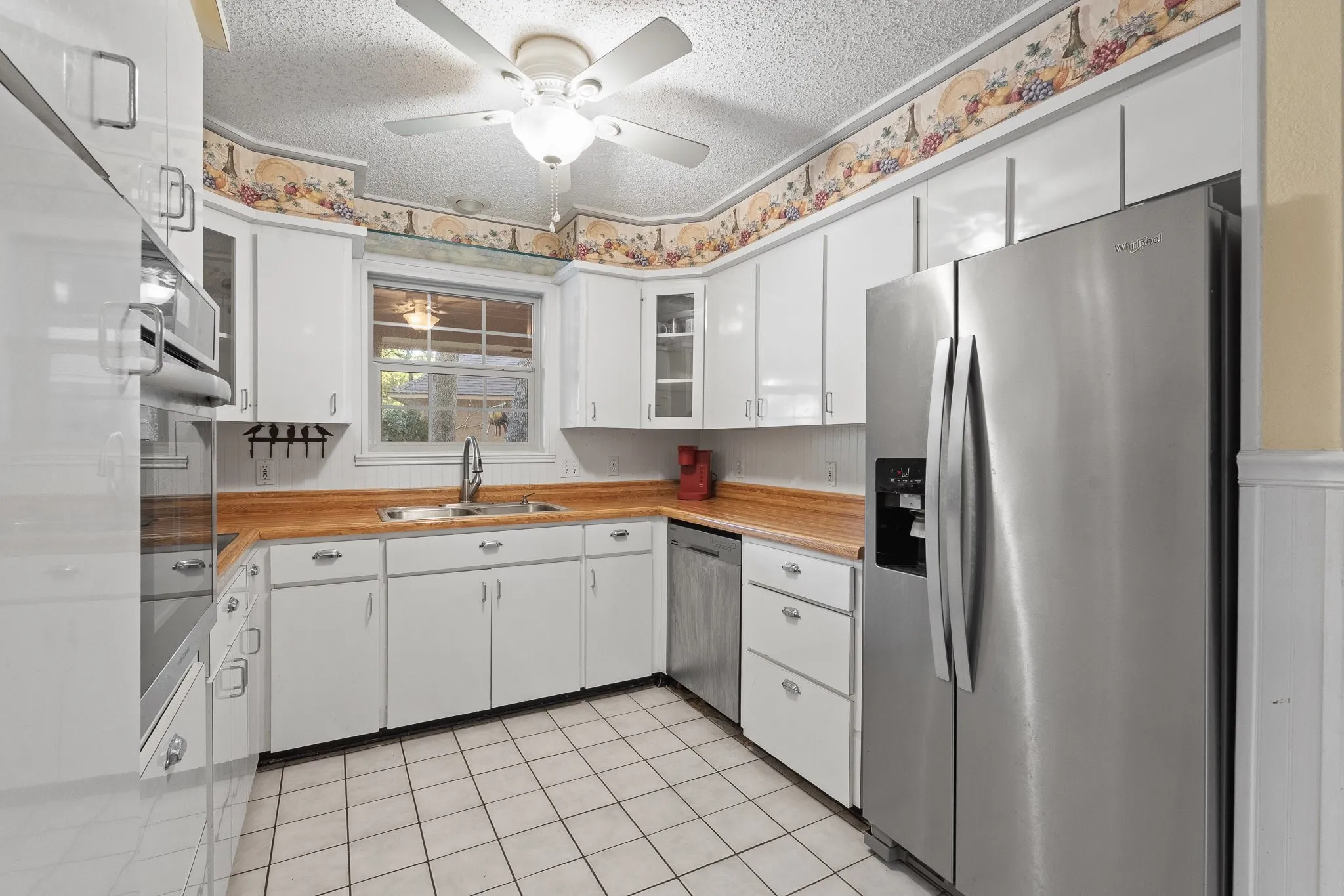 White cabinetry, wood-finish countertops, stainless steel appliances, ceramic tile flooring, and a ceiling fan with light fixture
