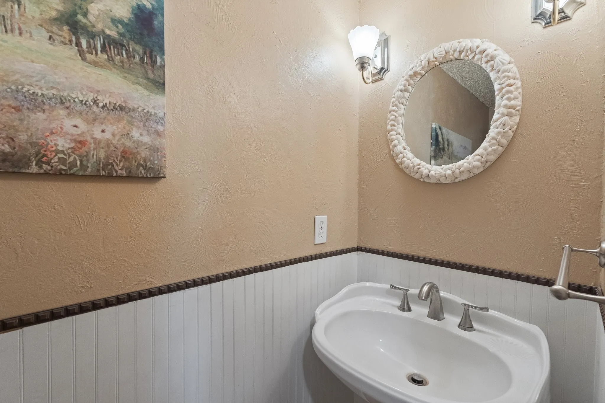 White beadboard wainscoting with decorative trim, pedestal sink, and wall-mounted sconce lighting