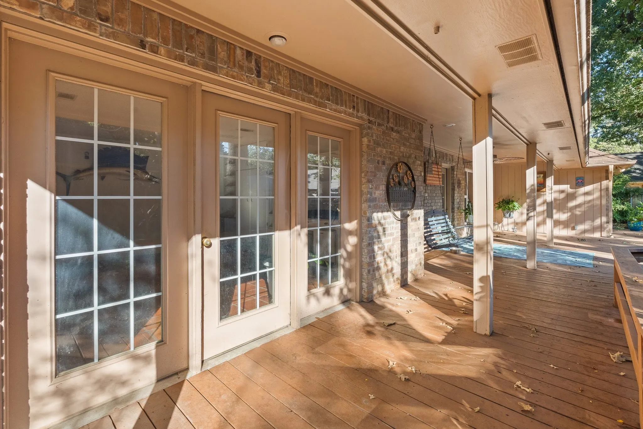 Expansive wooden deck with a covered patio featuring brick siding and multiple support pillars