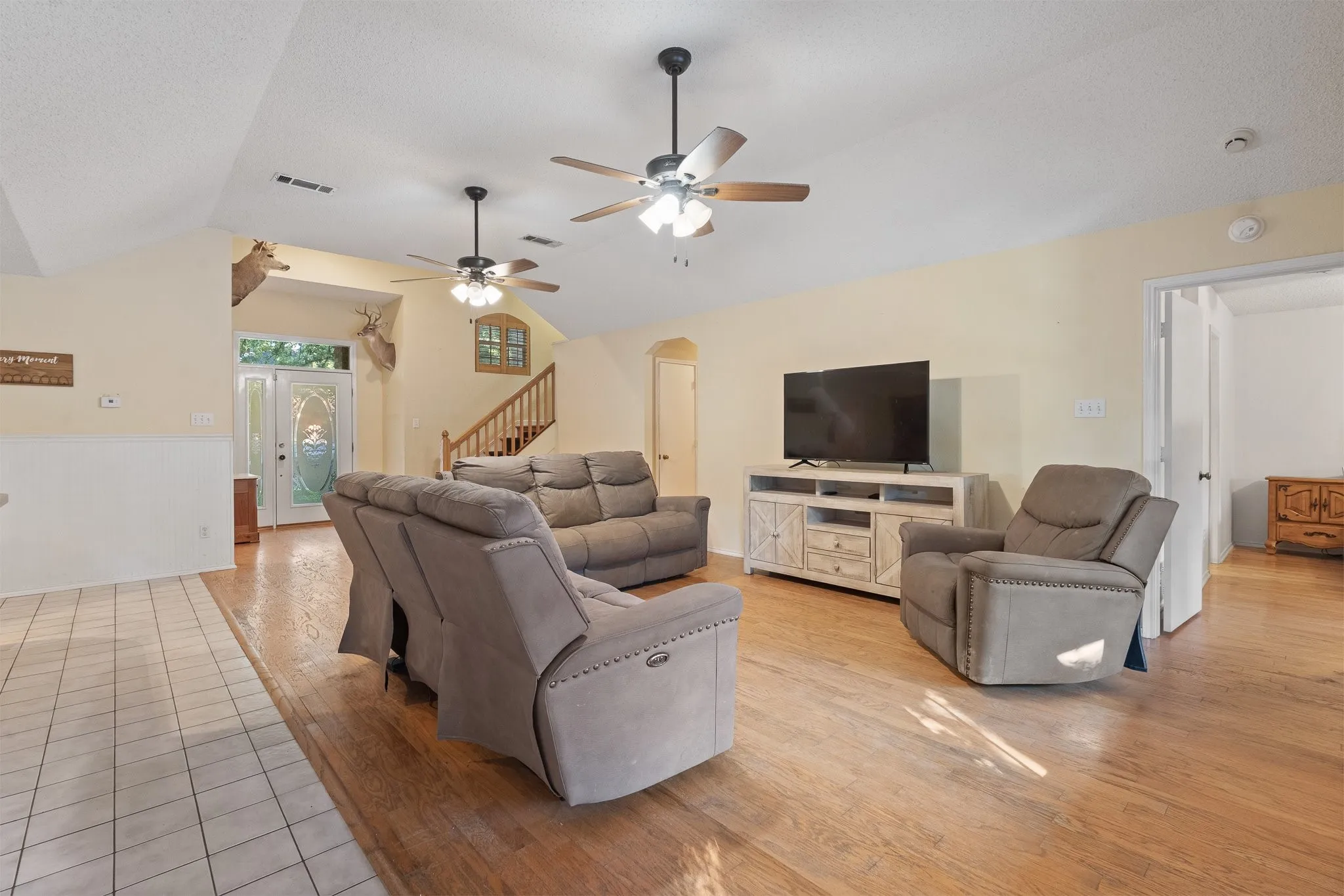 Vaulted ceiling with multiple ceiling fans, wood-finish flooring, wainscoting, and a decorative front entry door