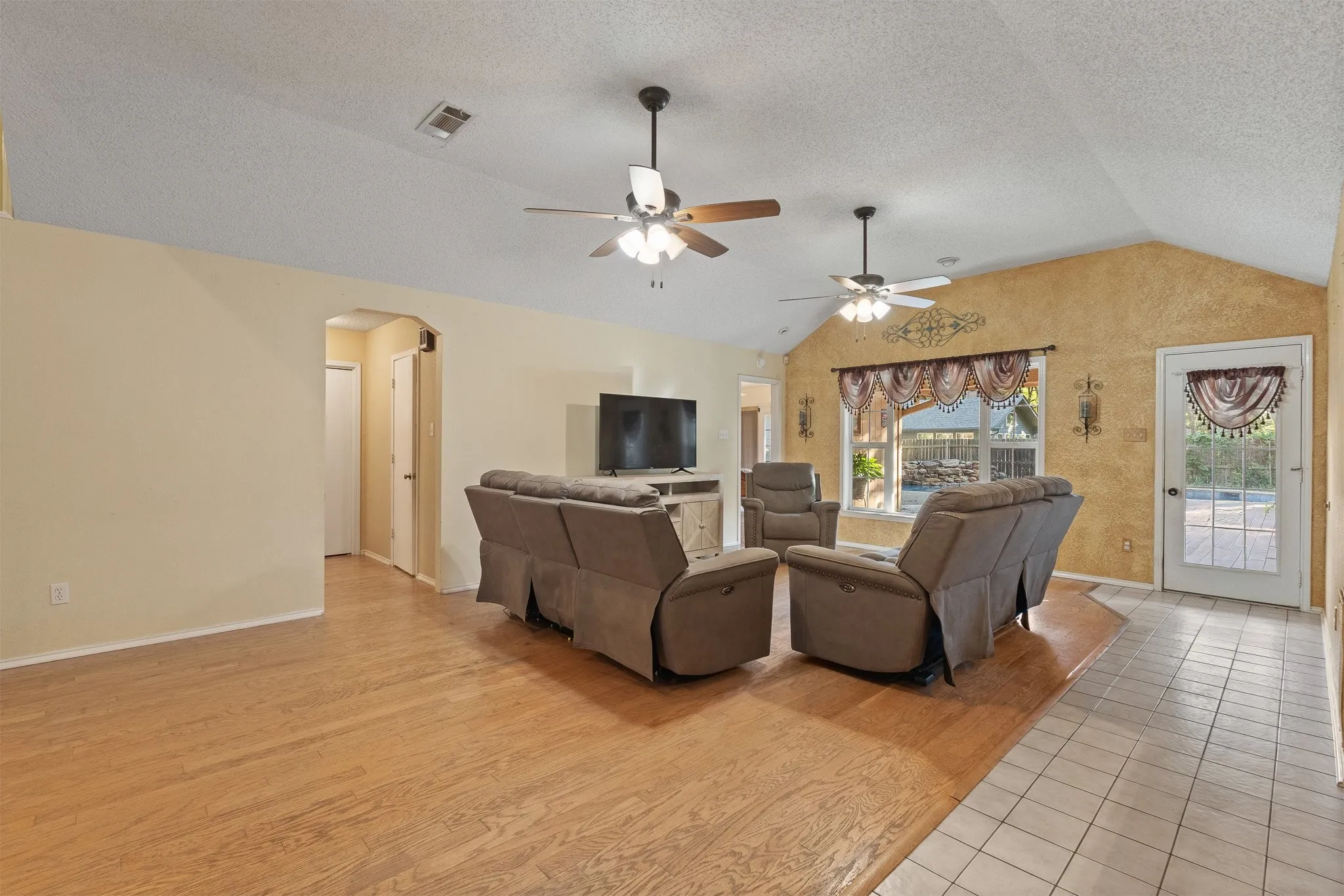 Vaulted ceilings with ceiling fans, wood-finish flooring, tile flooring, and a glass-paneled exterior door