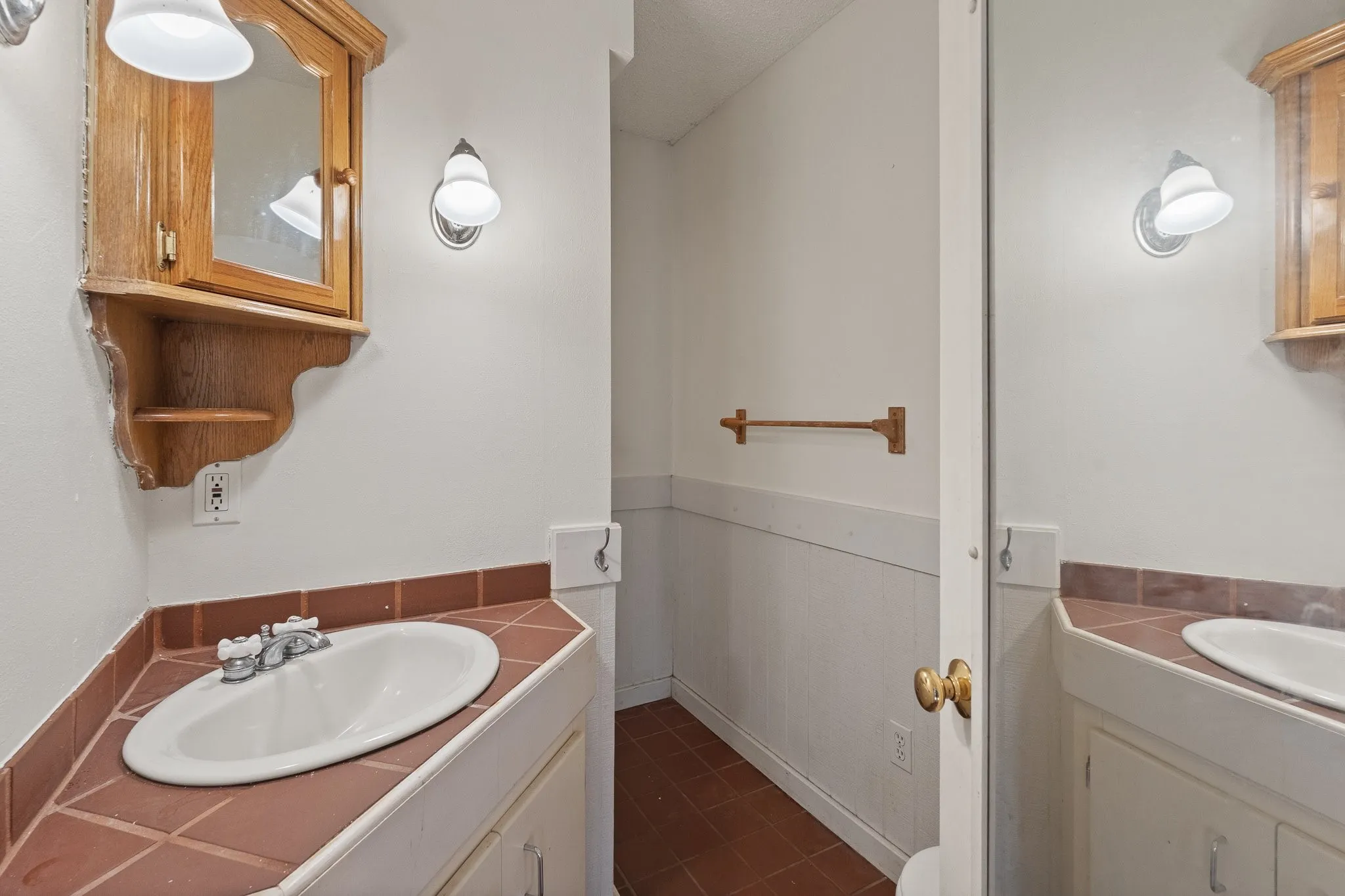 Vanity with tile countertop, integrated sink, and wall-mounted sconce lighting