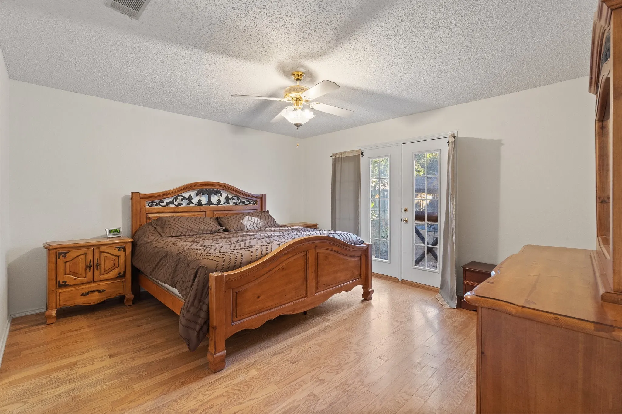 Light wood-finish flooring, white walls, ceiling fan, and double French doors with transom windows