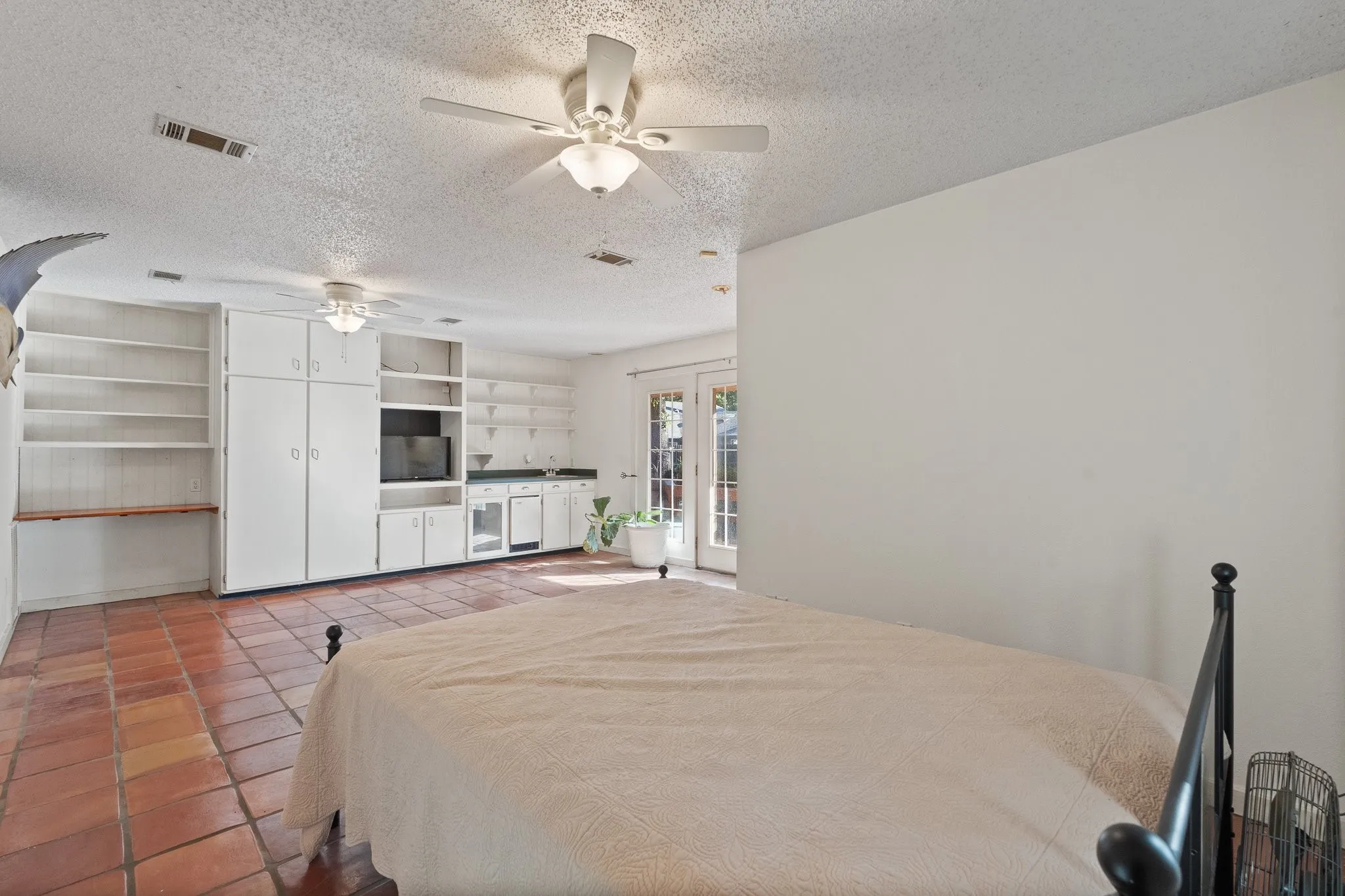 Terracotta tile flooring, built-in shelving, white cabinetry, ceiling fans, and a built-in wet bar