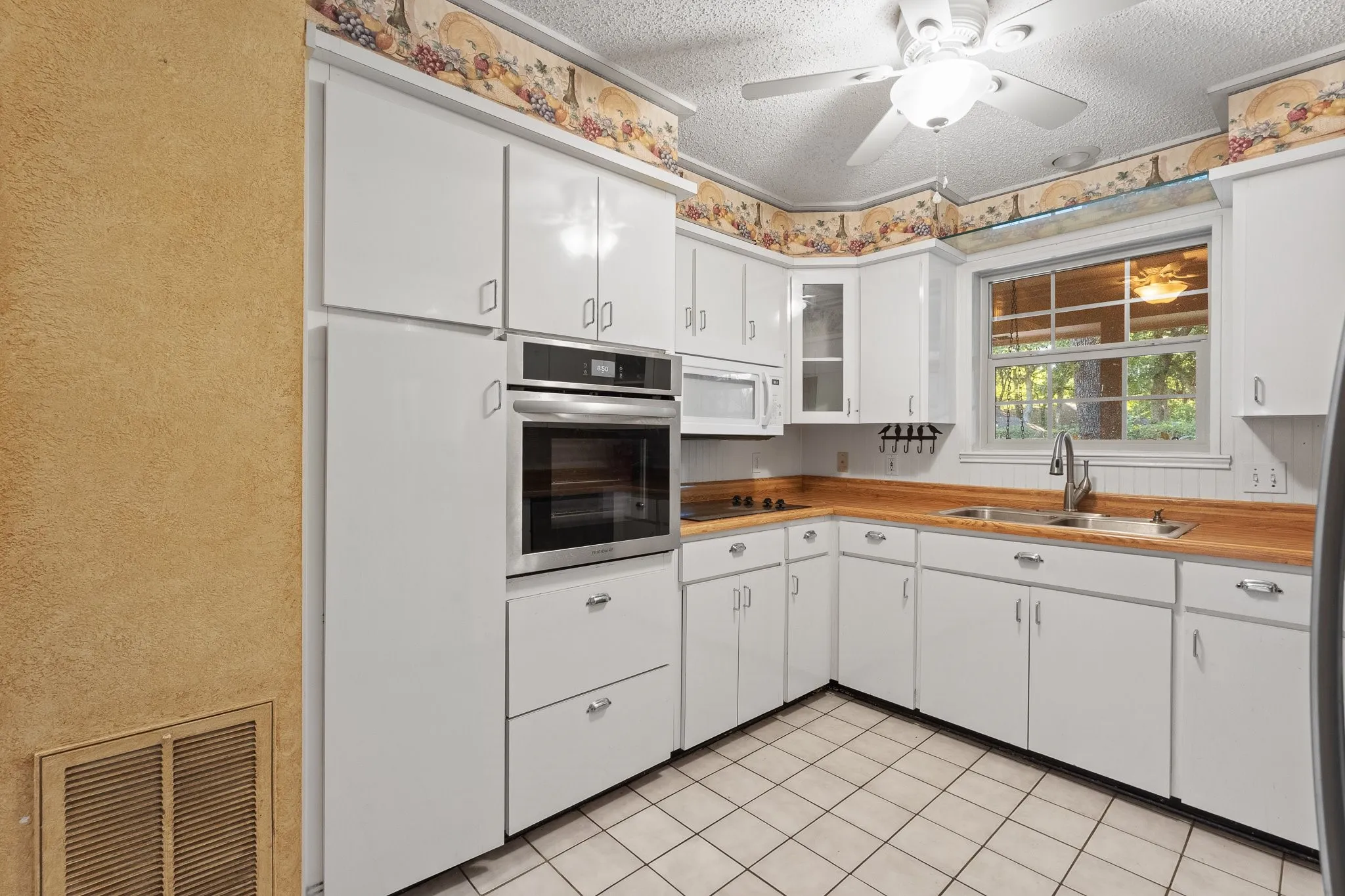 White cabinetry with brushed nickel hardware, wood-finish countertops, stainless steel built-in oven, white tiled flooring, and a ceiling fan