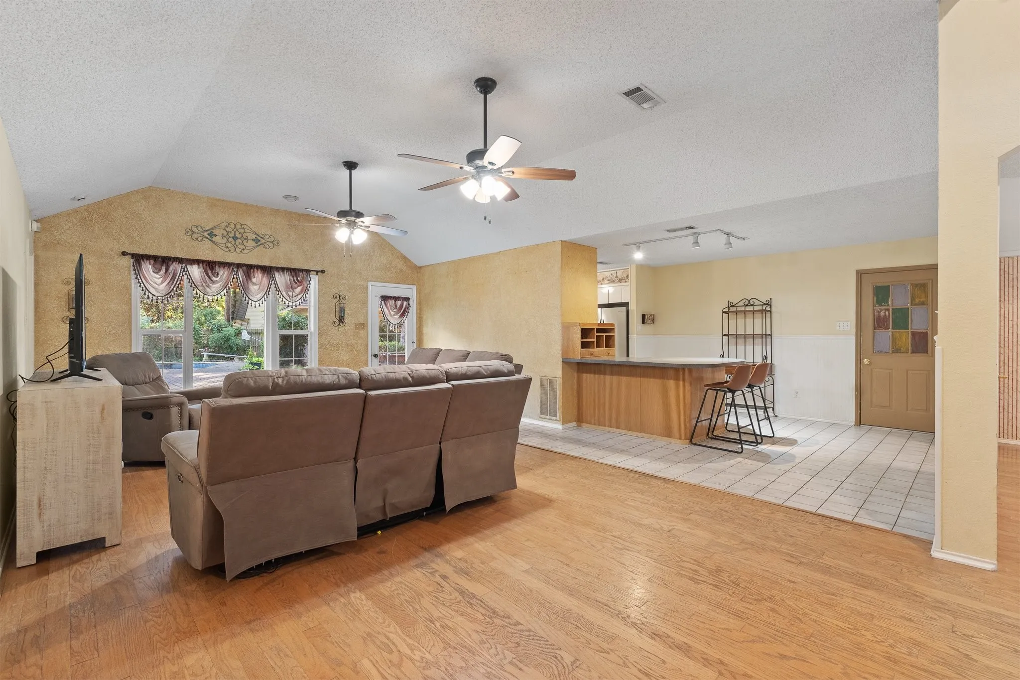 Vaulted ceiling, wood-finish flooring, ceiling fans, built-in bar, and track lighting