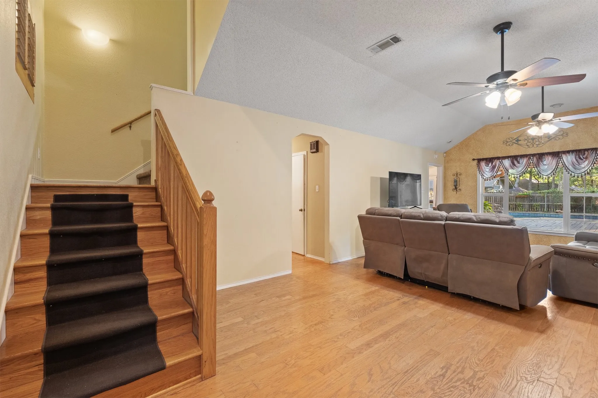 Wood-finish flooring throughout, vaulted ceiling, dual ceiling fans, and a staircase with wood railing and carpet runner