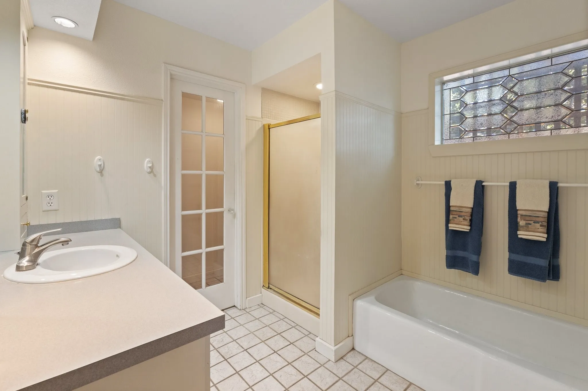 Full bathroom featuring a single vanity, integrated tub, glass-enclosed shower, and a decorative transom window
