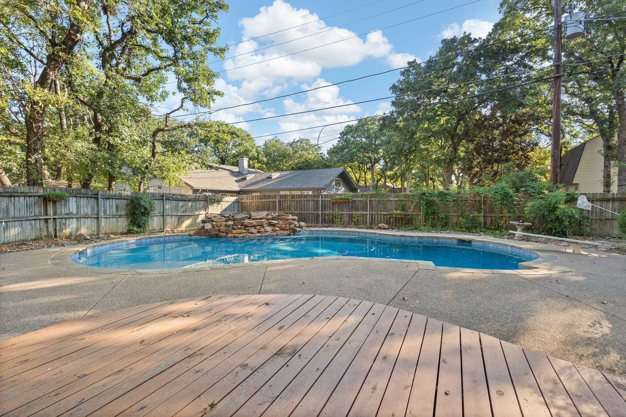 In-ground swimming pool featuring a rock waterfall, surrounded by a concrete patio and a wooden deck
