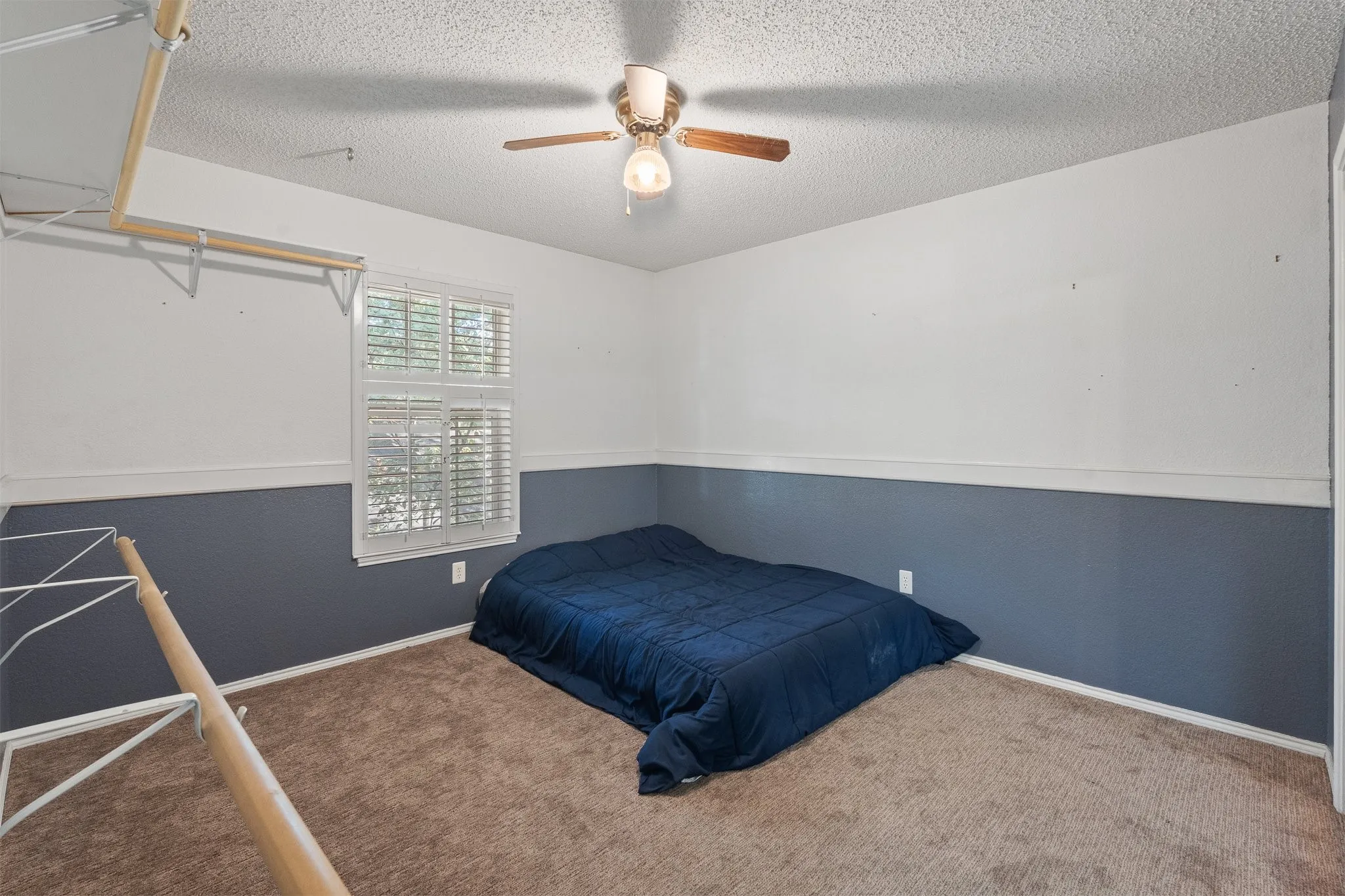 Window with horizontal blinds, overhead ceiling fan, and wall-mounted wooden rods
