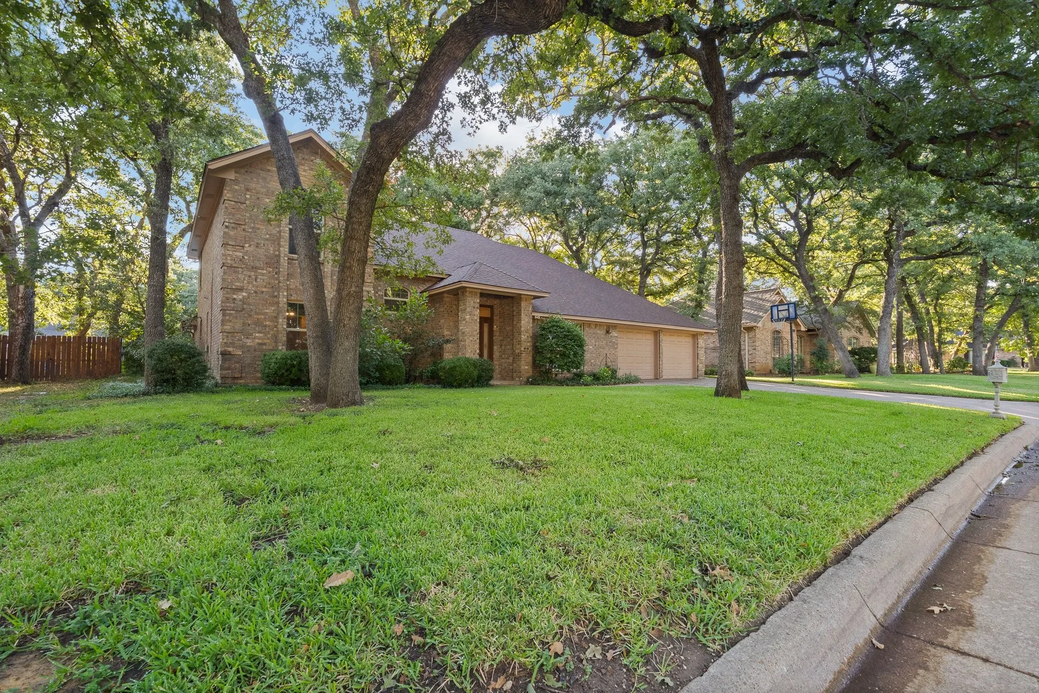 Brick exterior residence with a multi-car garage, mature trees, and a manicured lawn
