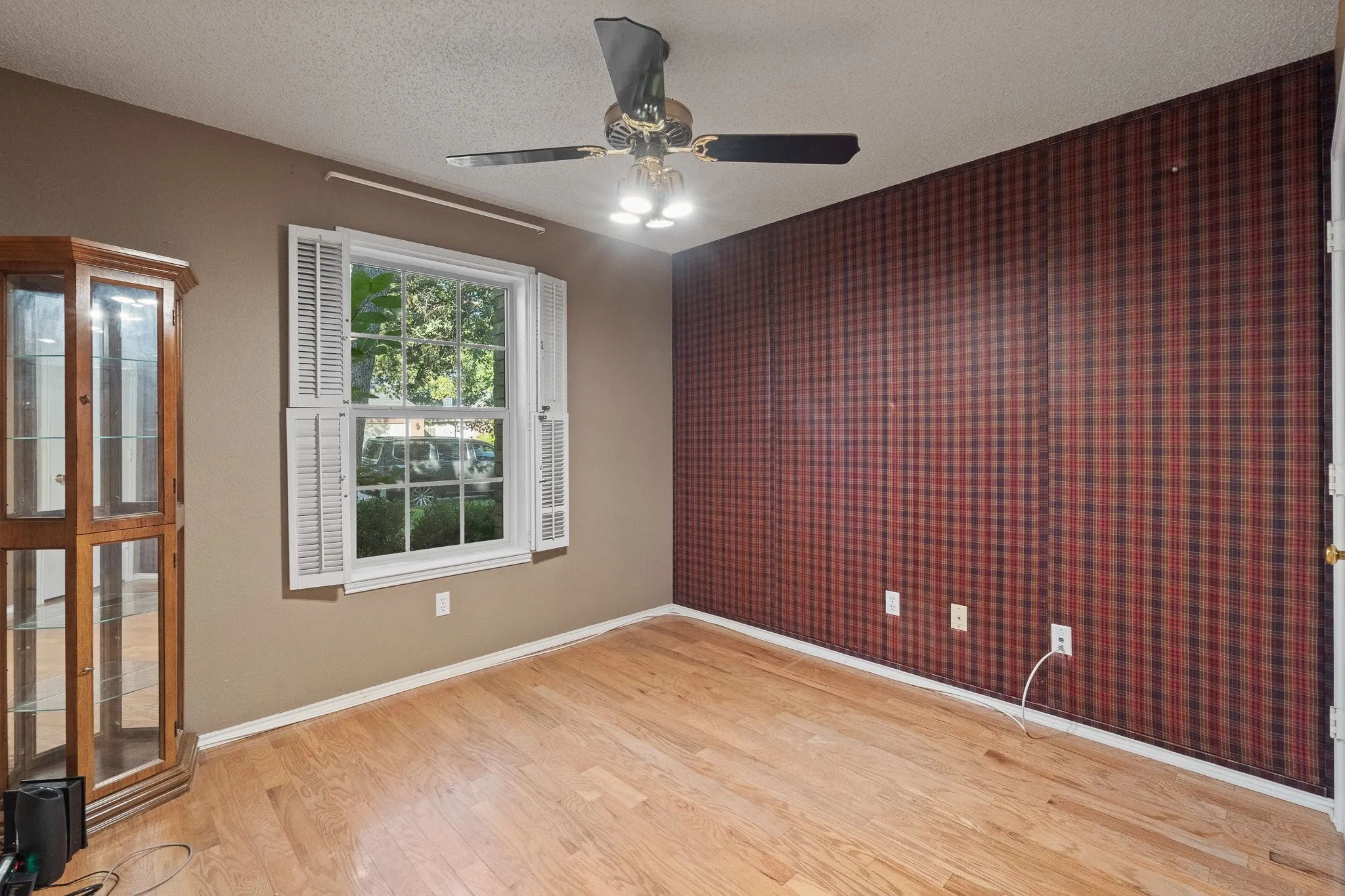 Hardwood flooring, window with white plantation shutters, ceiling fan with integrated lighting, patterned accent wall