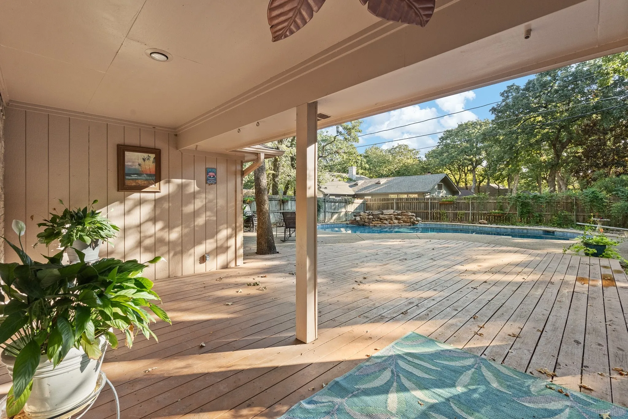 Covered patio with recessed lighting, wood-plank decking, and a fenced swimming pool featuring a rock waterfall