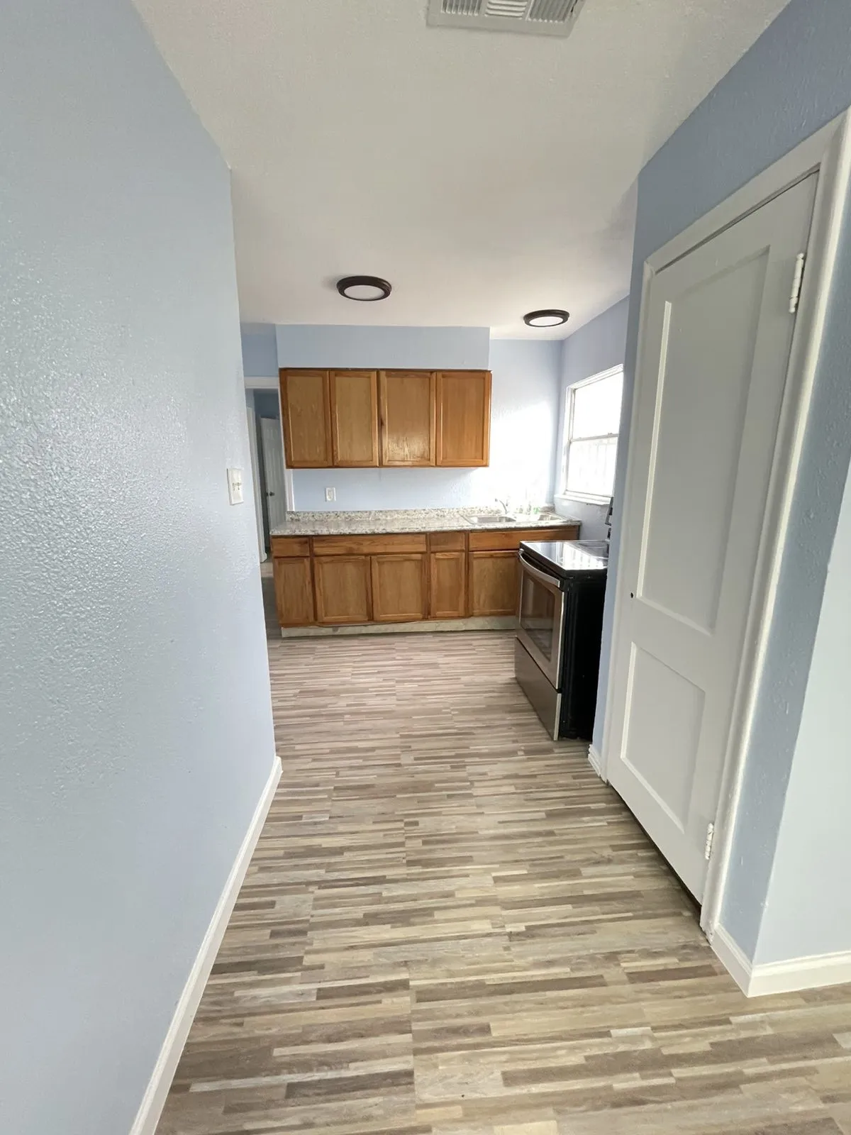 Kitchen featuring wood finish cabinets, electric stove, light wood-style flooring, light countertops, and a textured wall