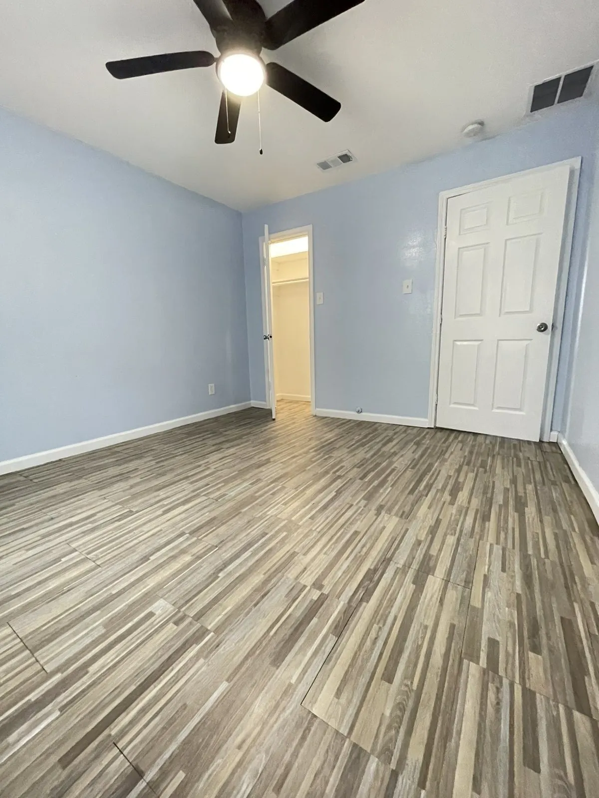 Unfurnished bedroom with light wood-type flooring, a spacious closet, and a ceiling fan