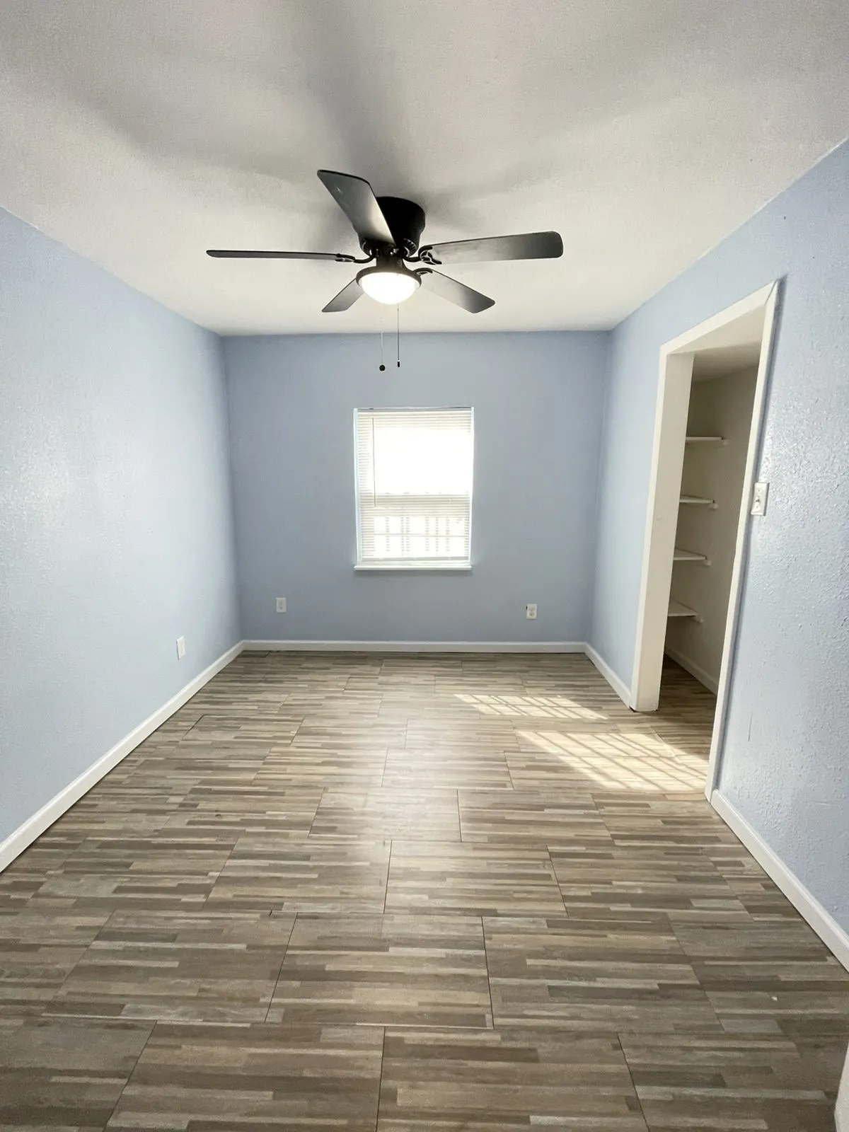 Unfurnished bedroom with ceiling fan, wood tiled floors, and a textured wall