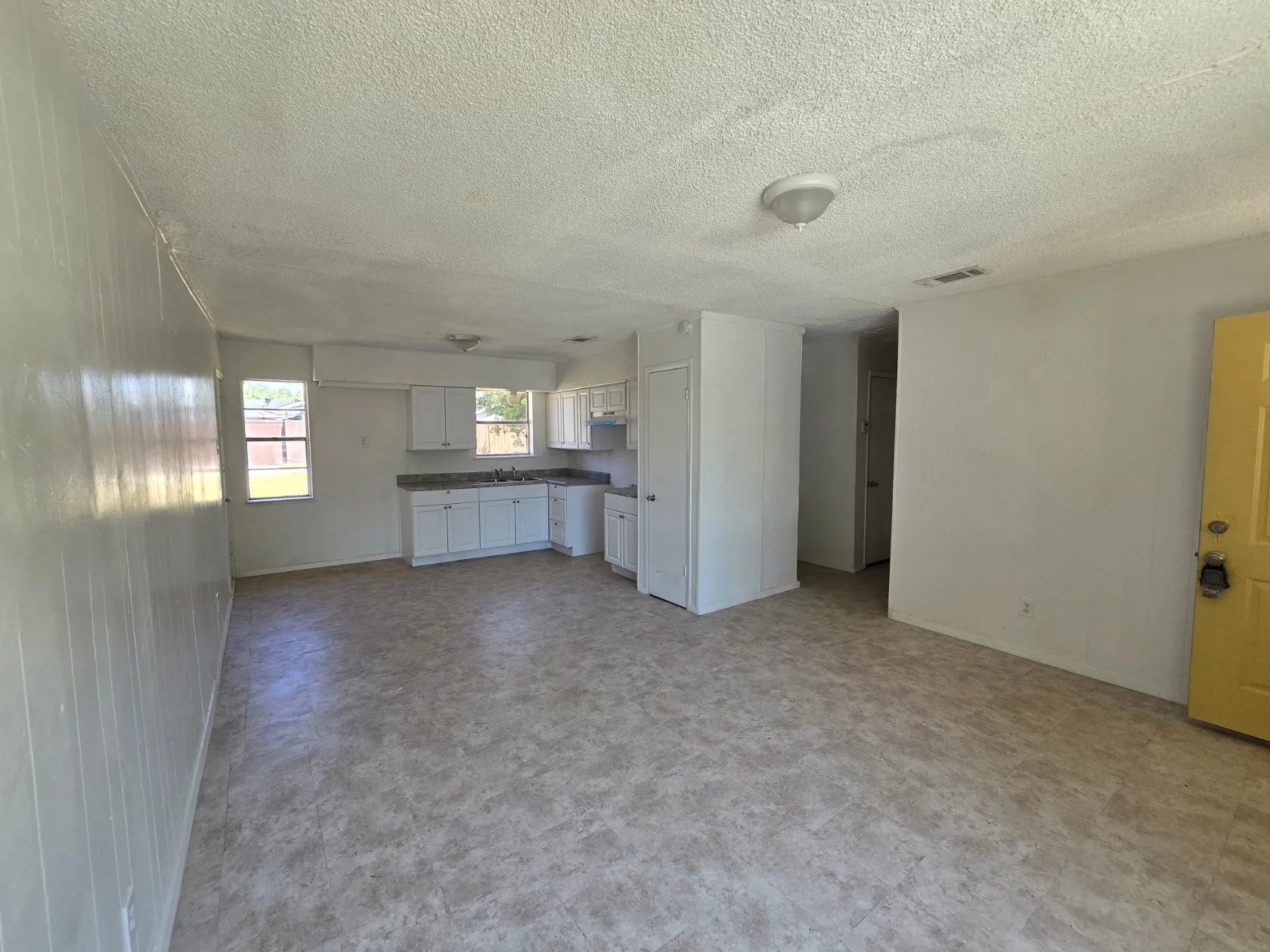 Open-concept living area with vinyl plank flooring, a kitchen featuring white cabinetry and laminate countertops, and multiple windows providing natural light