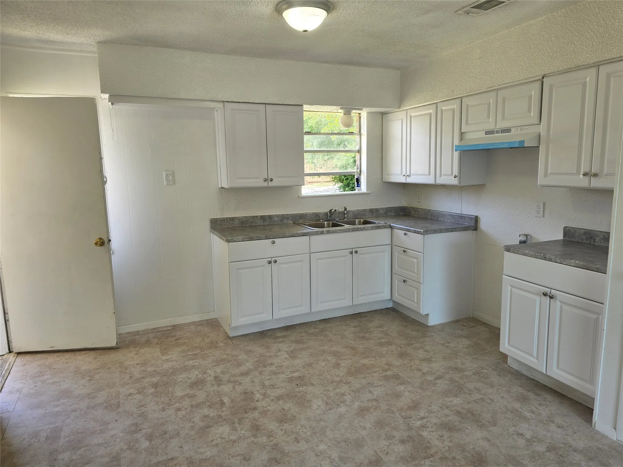 Kitchen featuring white cabinetry, gray speckled countertops, a double basin stainless steel sink, and light-toned linoleum flooring