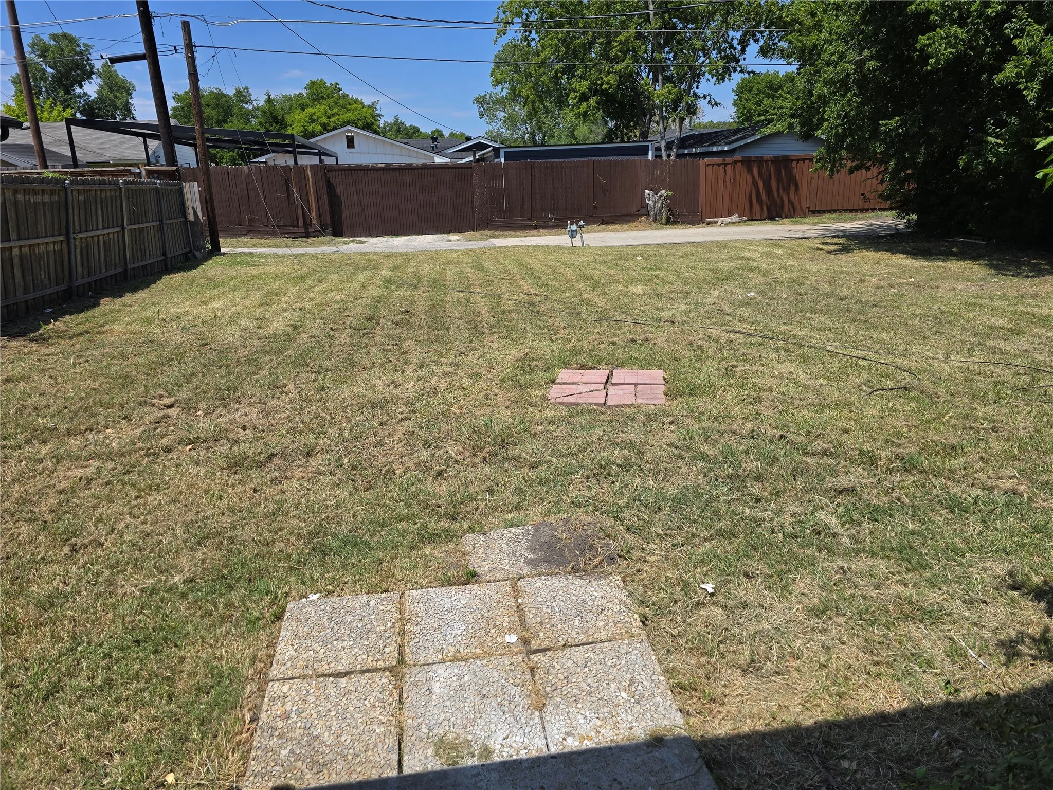 Expansive backyard featuring a brown privacy fence, a wood-slat fence, and a concrete paver patio area