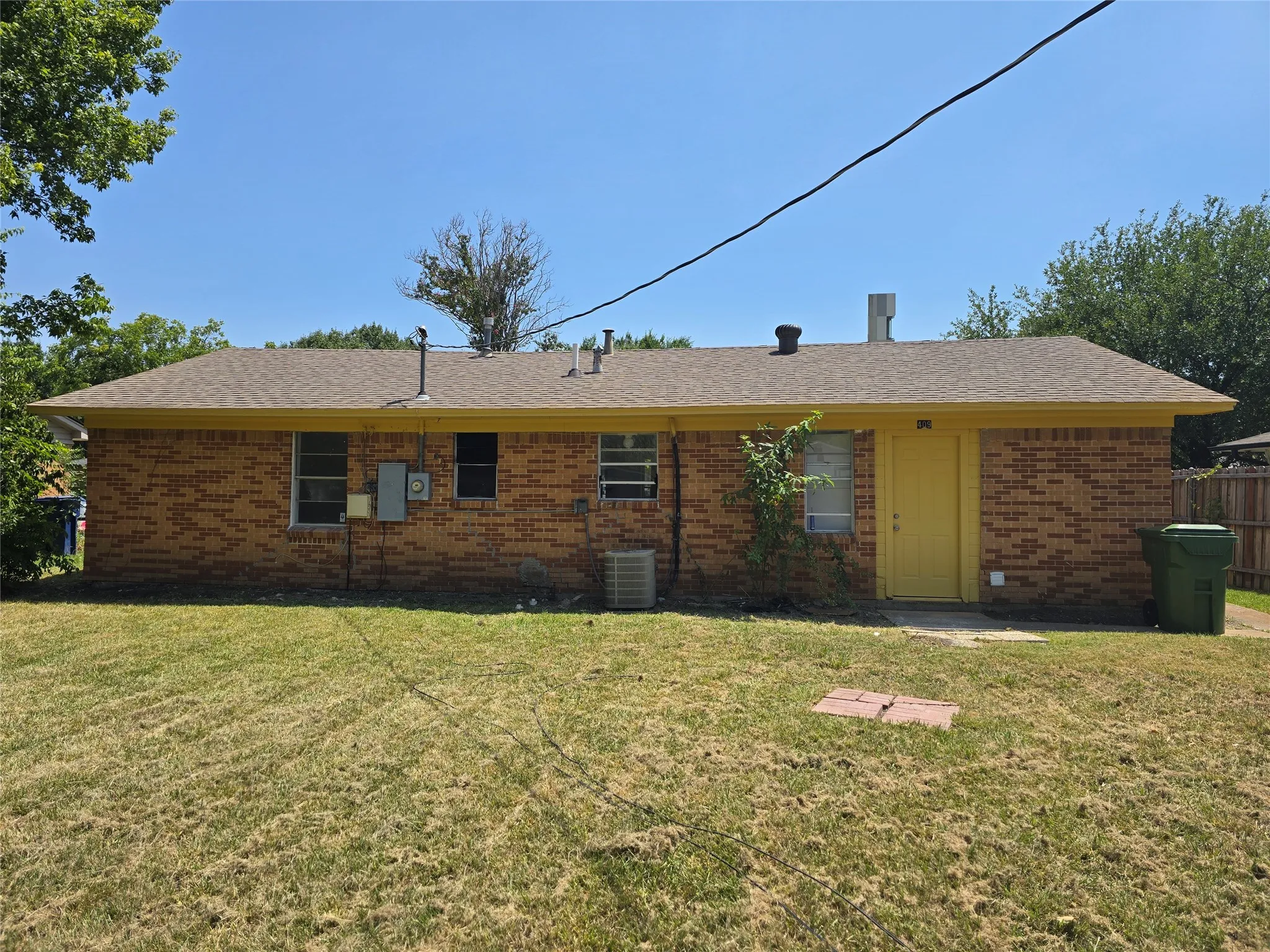 Brick exterior with a yellow door and a shingled roof