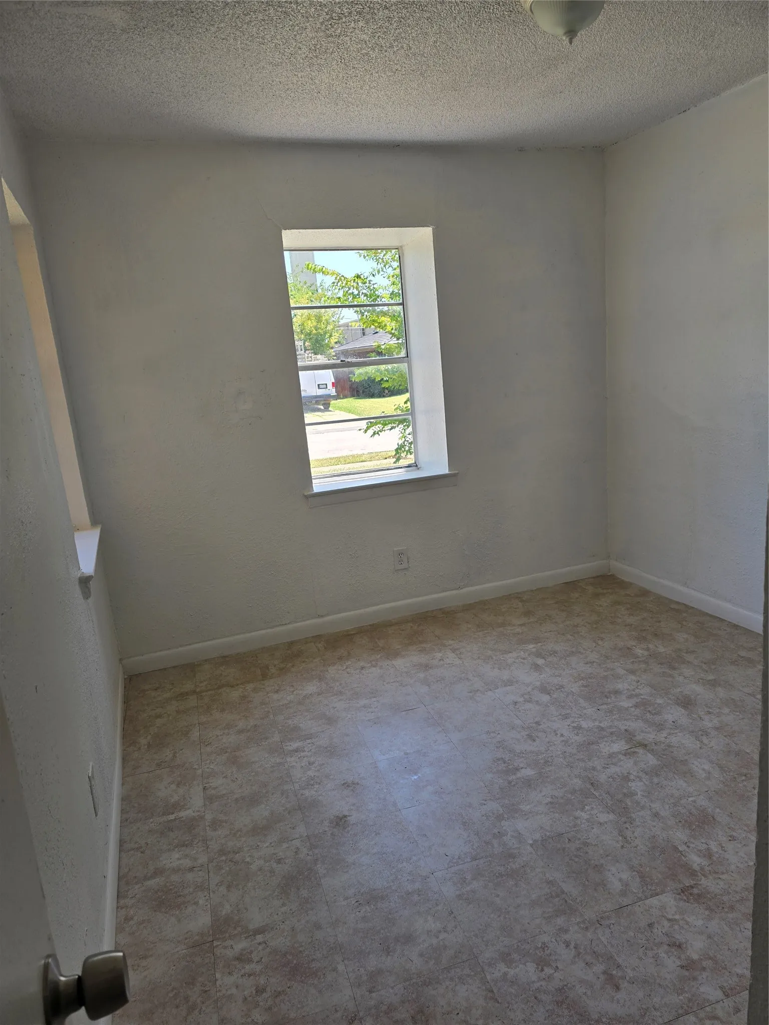 Neutral wall paint, textured ceiling, tile-look flooring, and a single window