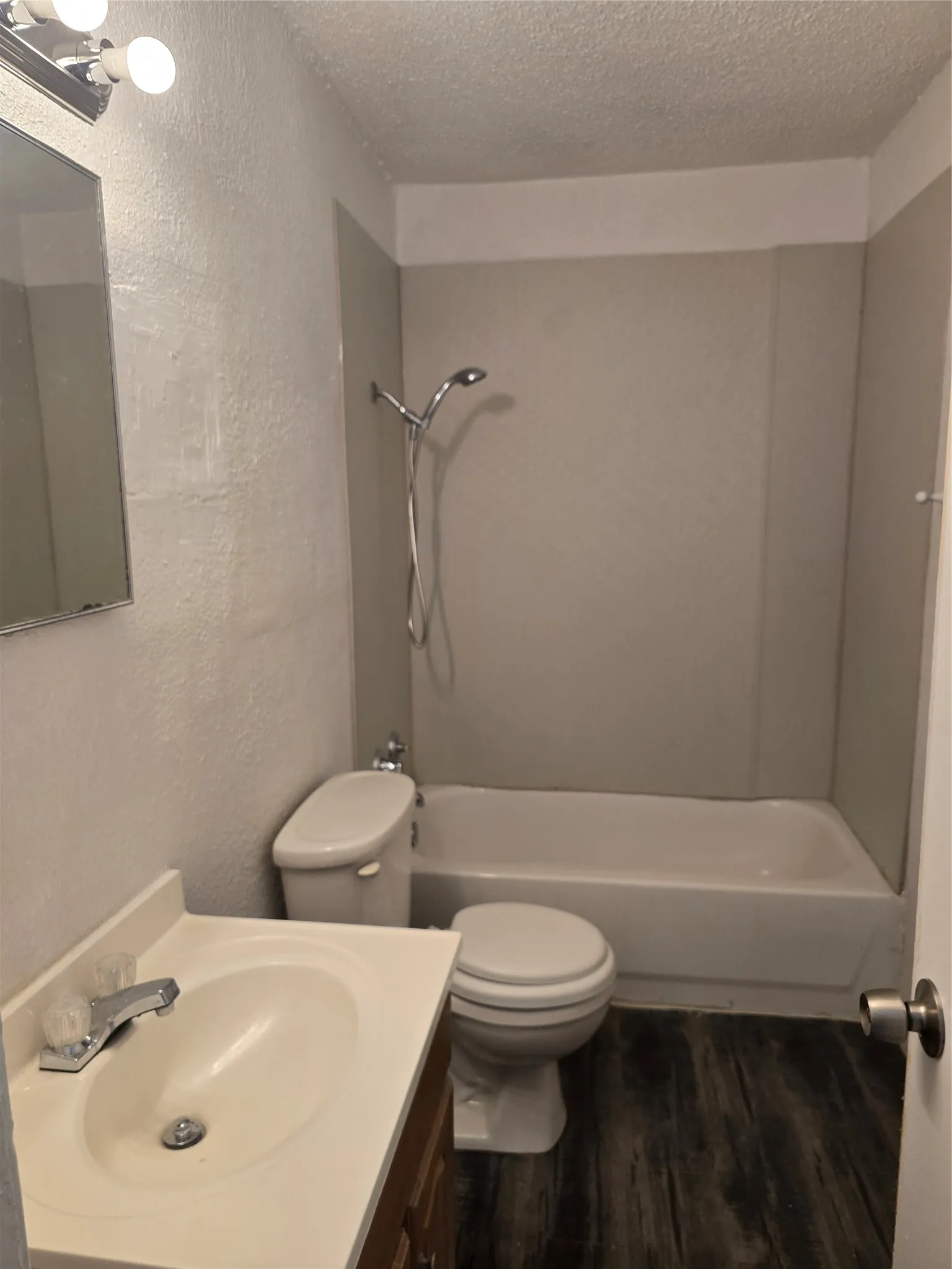 Bathroom featuring wood-finish flooring, a white vanity with an integrated sink, a built-in bathtub, and a shower with a chrome fixture