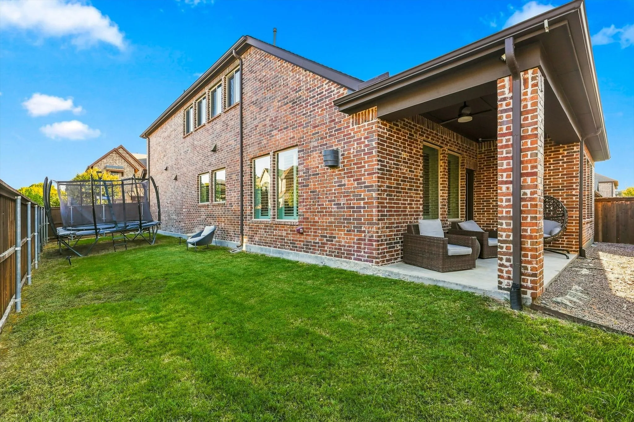 Brick exterior with multiple windows, covered patio with recessed lighting, and a fenced yard with a grass lawn