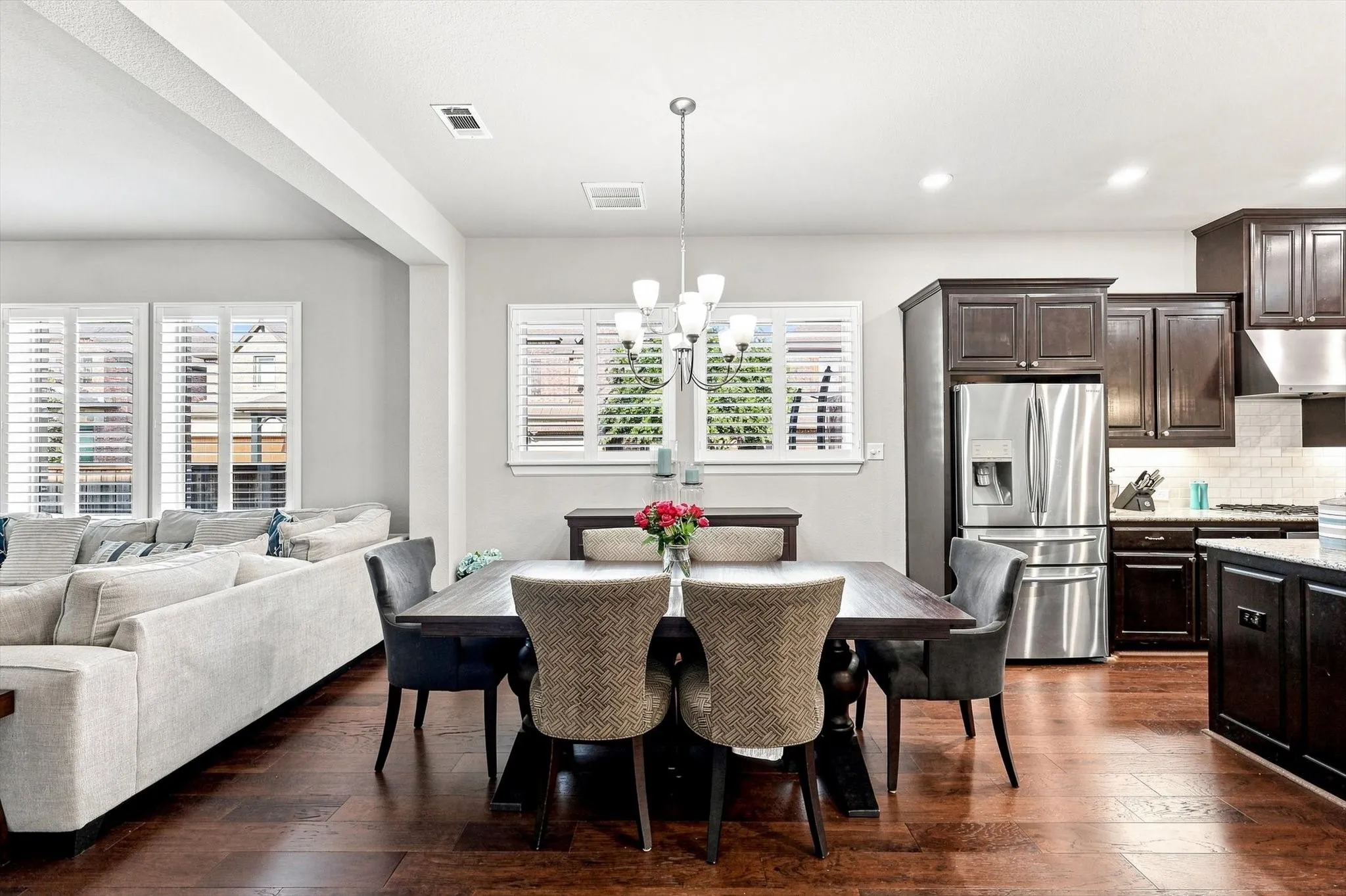 Open-concept living space with dark wood-finish flooring, white plantation shutters, and recessed lighting