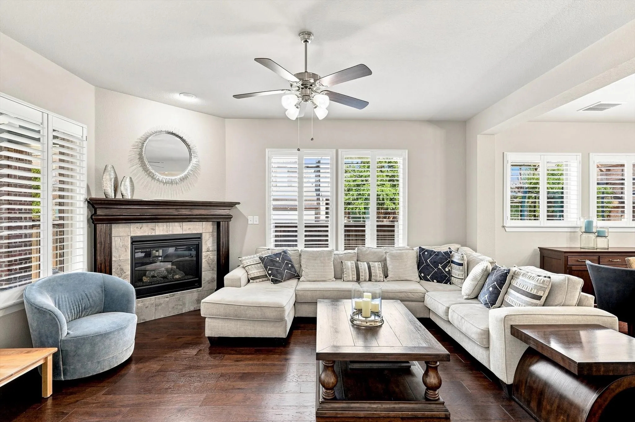 Living area featuring a corner fireplace with a wood mantel, wood-finish flooring, and white plantation shutters on multiple windows