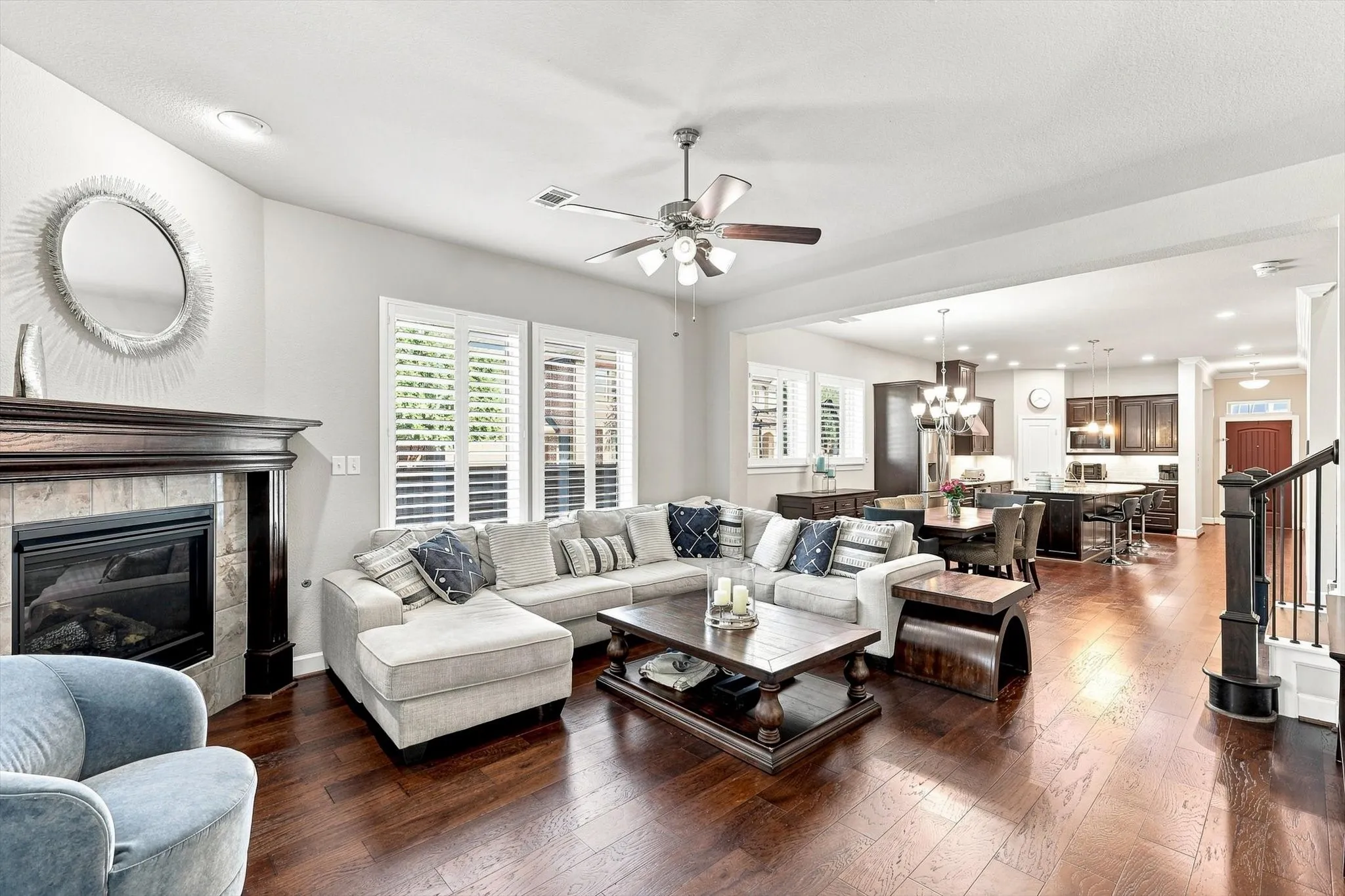 Hardwood flooring throughout, a gas fireplace with a decorative mantel, plantation shutters, a ceiling fan, and recessed lighting