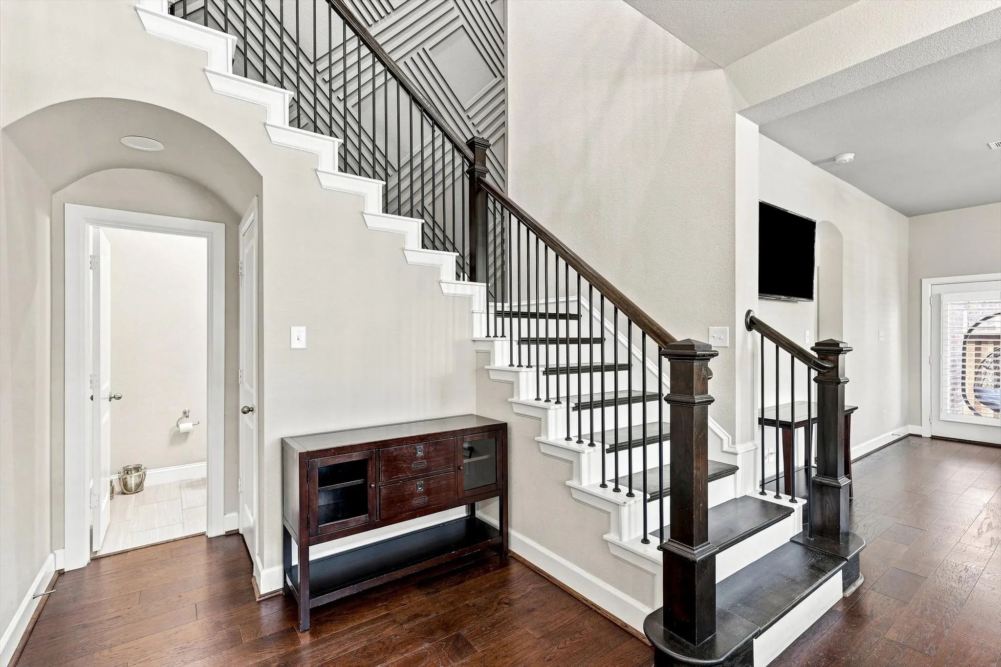 Rich wood-finish flooring, staircase with dark wood-finish handrail and black iron balusters, recessed lighting, arched doorway, and built-in wall niche