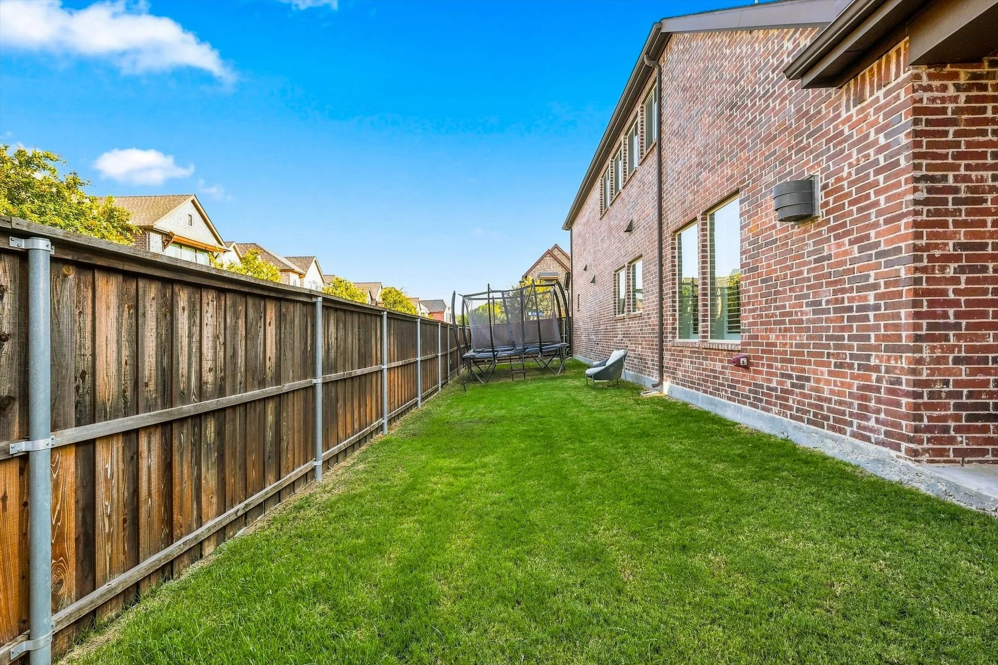 Red brick exterior with multiple windows, a wood fence, and a green lawn
