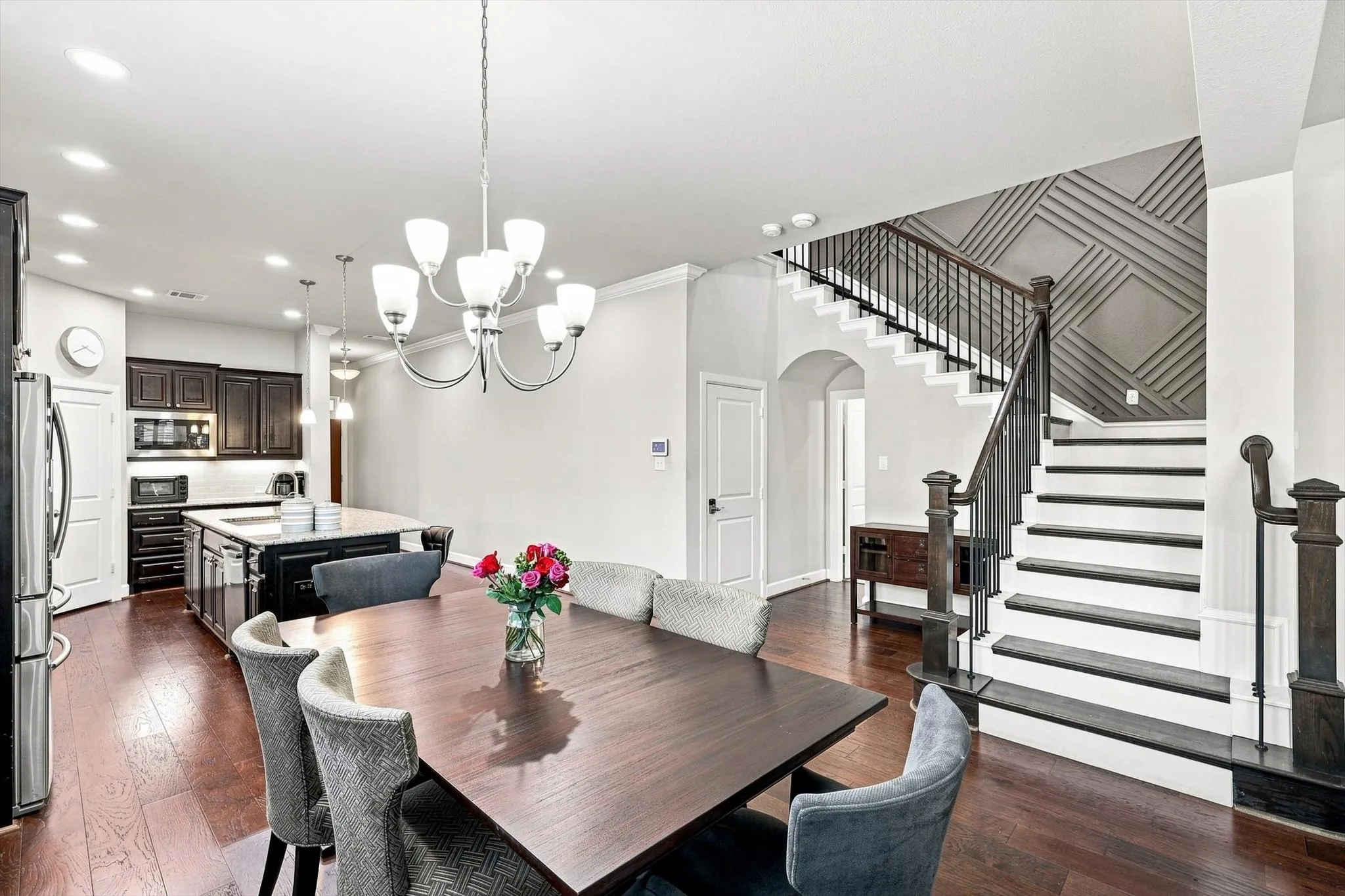 Hardwood flooring throughout, kitchen island with built-in storage, stainless steel appliances, chandelier lighting, and a staircase with decorative wall paneling