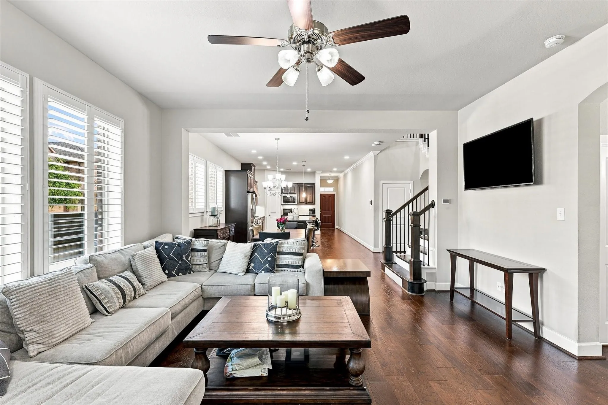 Hardwood-finish flooring throughout, ceiling fan with light fixture, custom window shutters, archway details, and staircase with dark wood banister