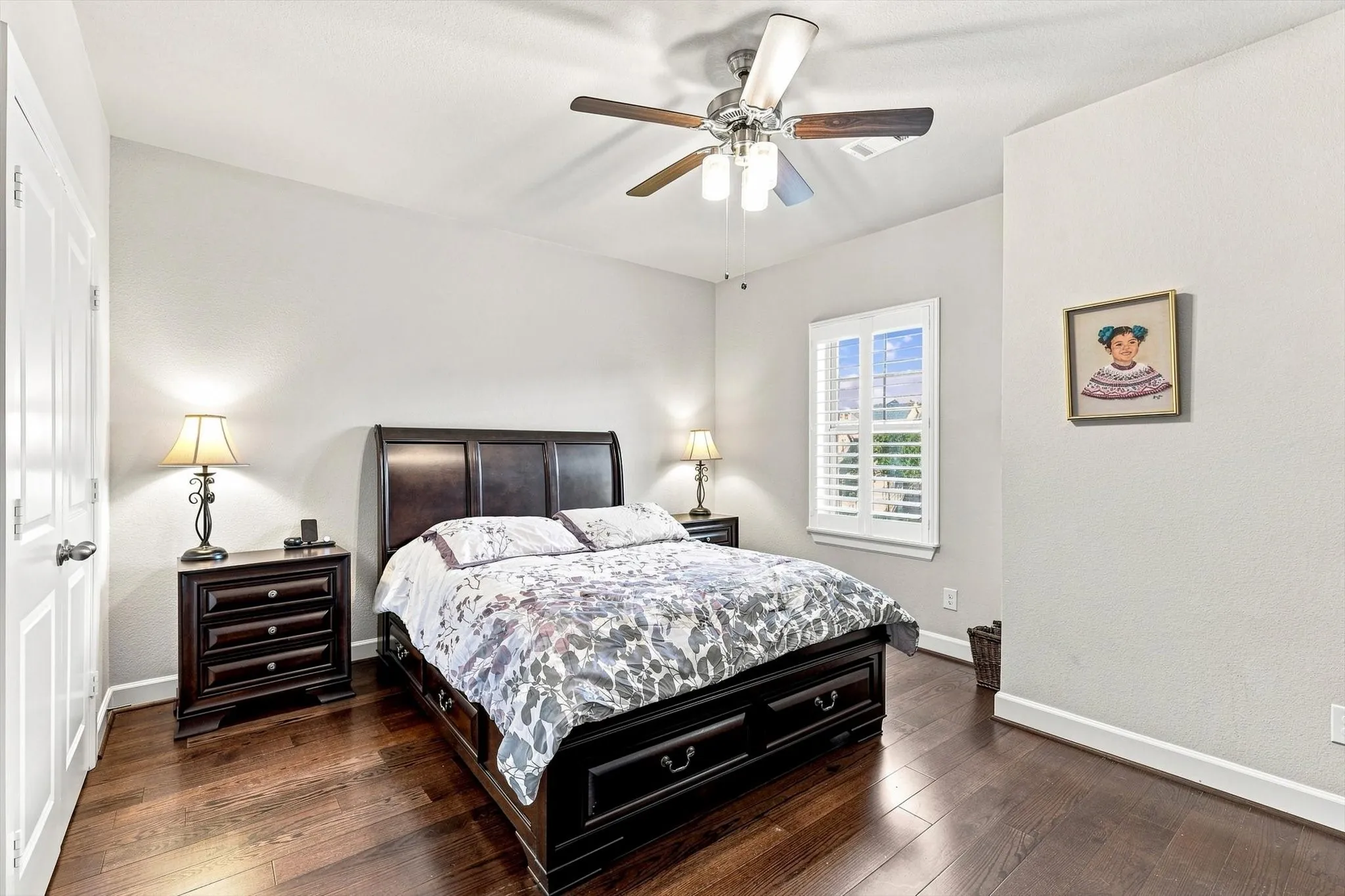 Hardwood flooring, window with plantation shutters, ceiling fan, and white painted walls