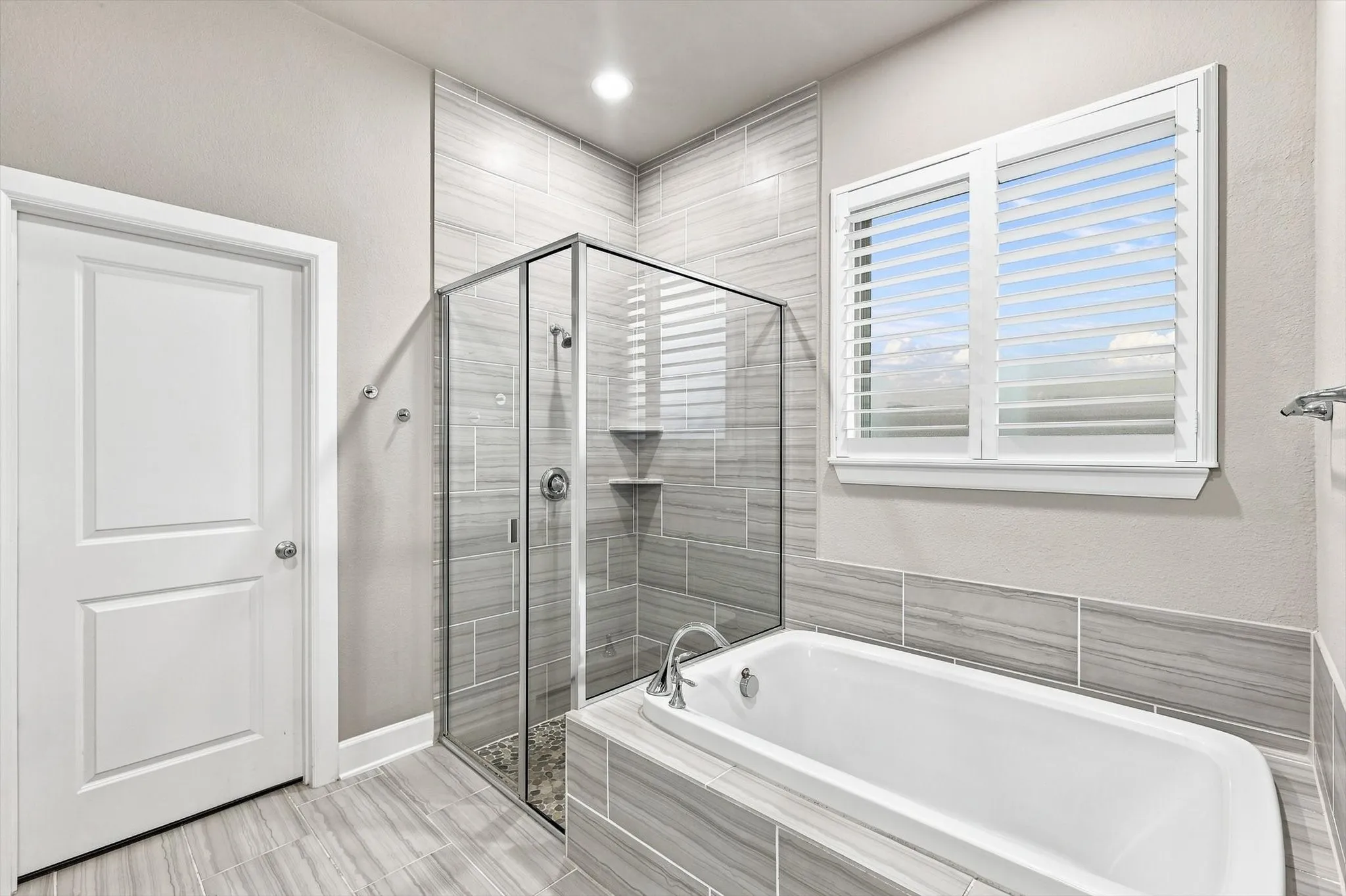 Built-in bathtub with tiled surround, glass-enclosed shower, wall-mounted showerhead, and tile flooring