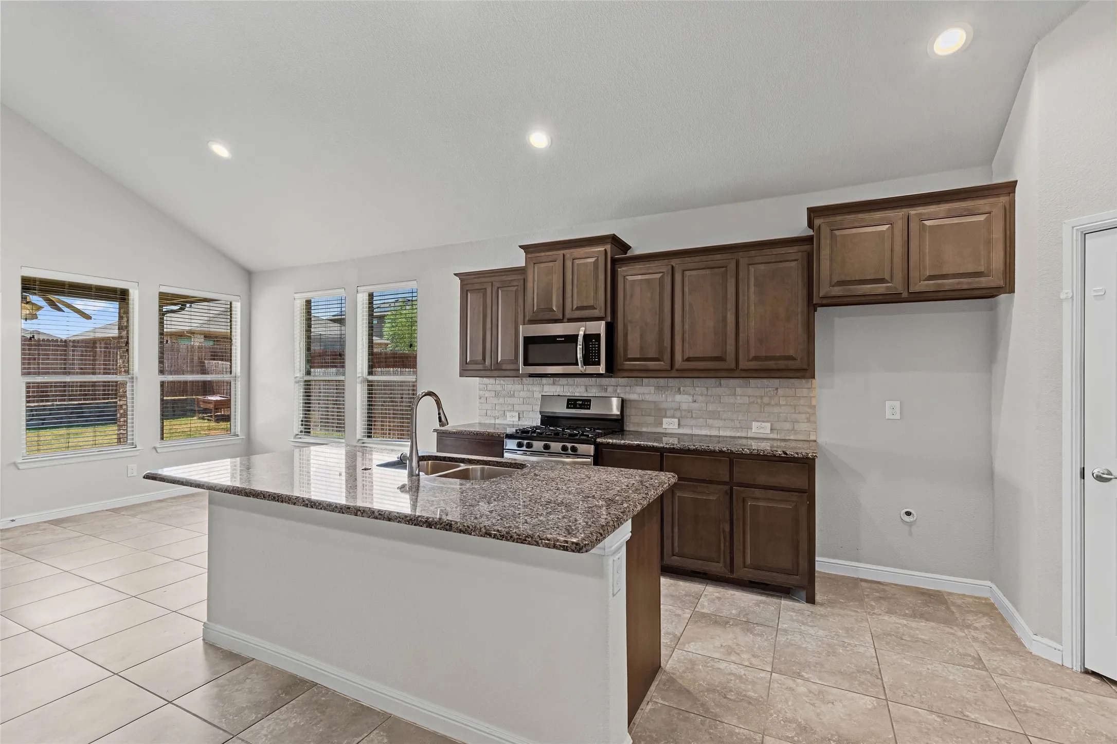 Kitchen featuring a central island with a sink, stainless steel appliances, dark wood cabinetry, and recessed lighting
