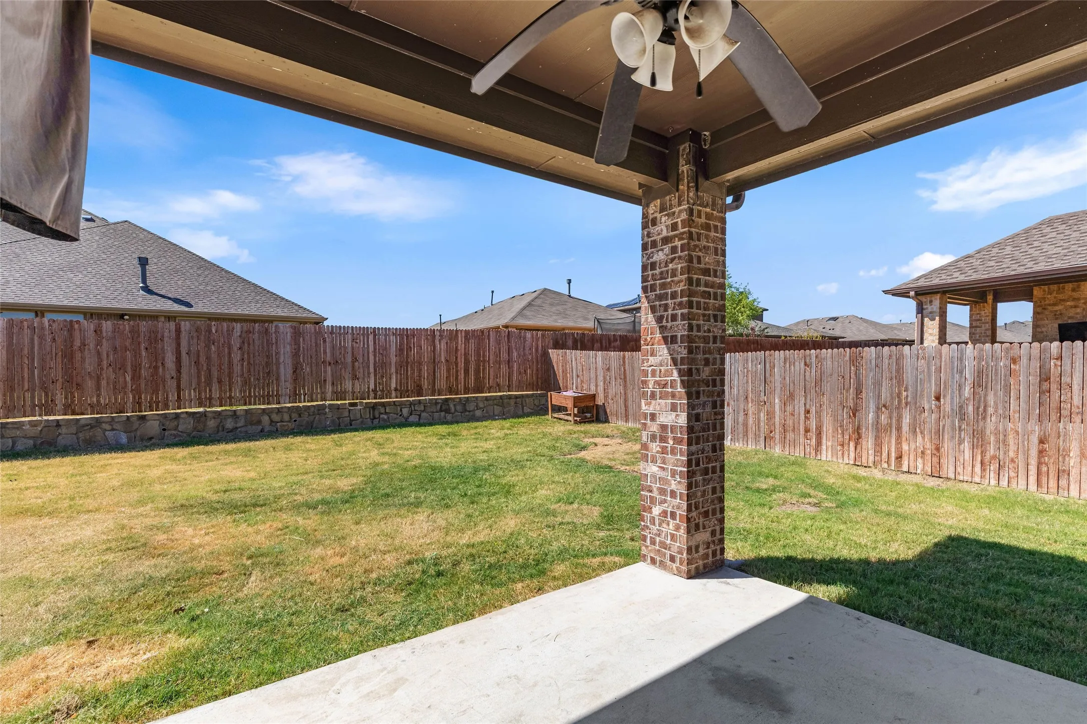 Covered patio with a ceiling fan, brick column, and concrete flooring